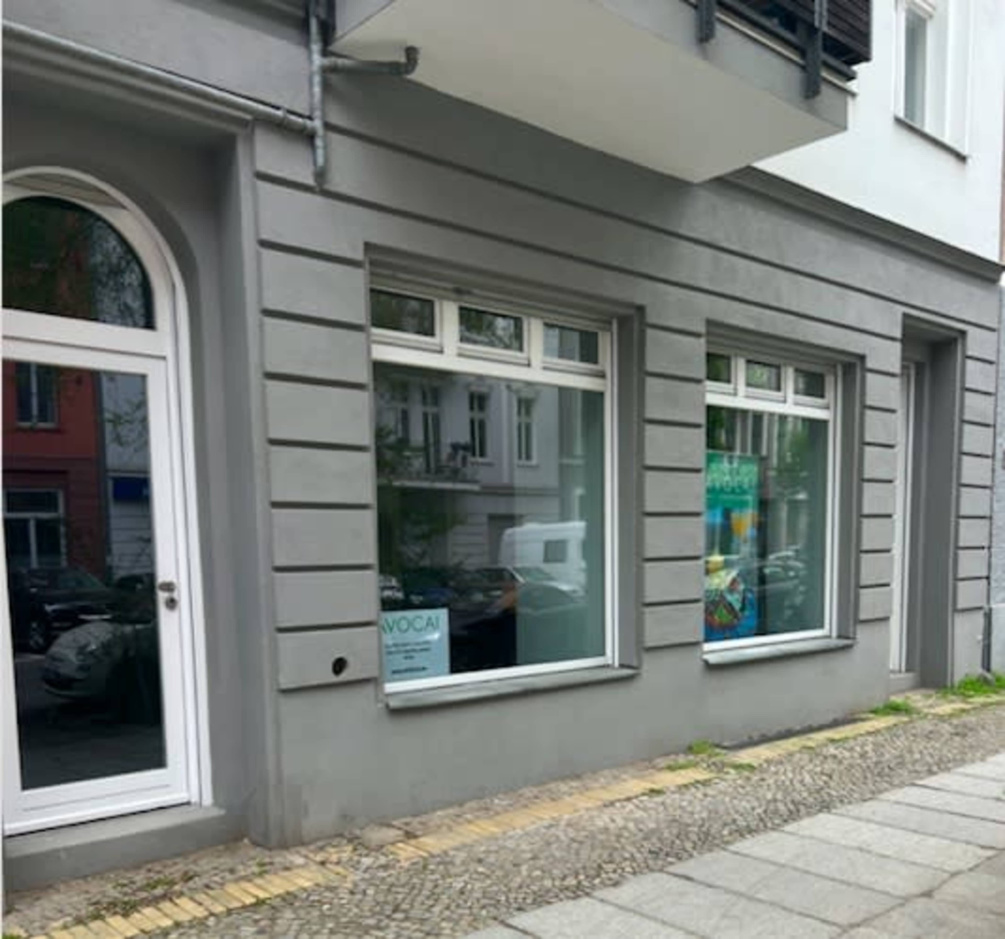 A gray building with a decorative entrance and two large windows displaying signs and posters.