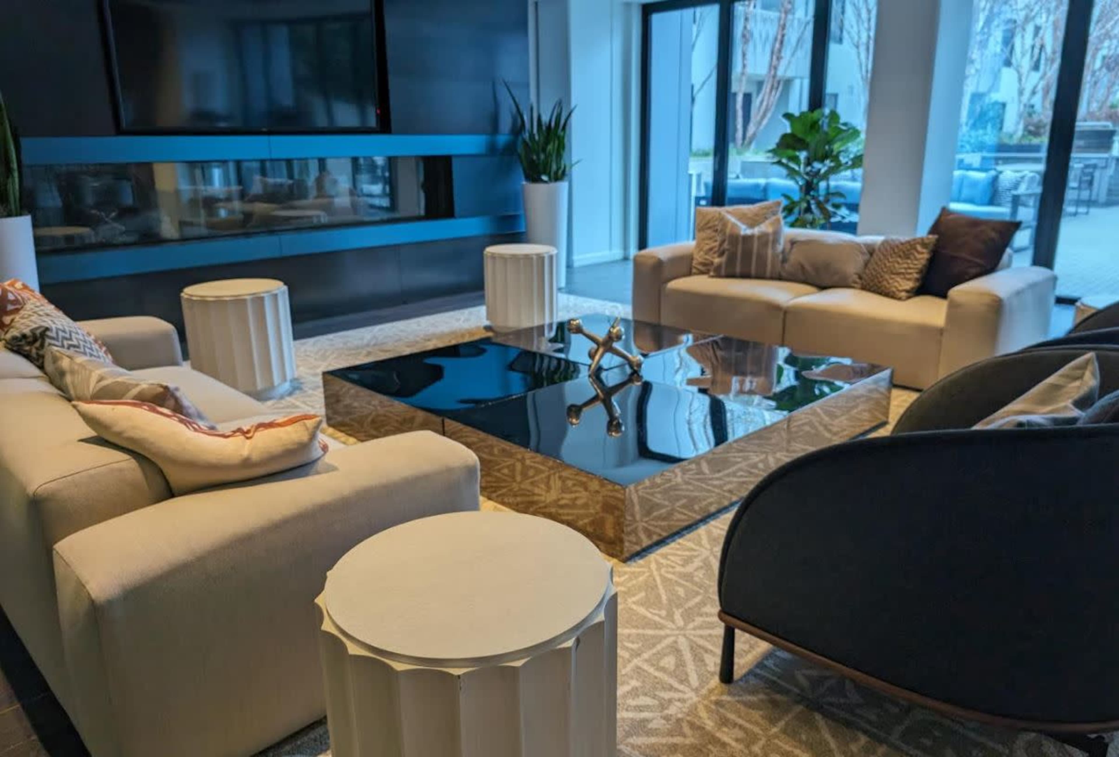 A modern living room with a black glass coffee table, beige sofas, and decorative plants.