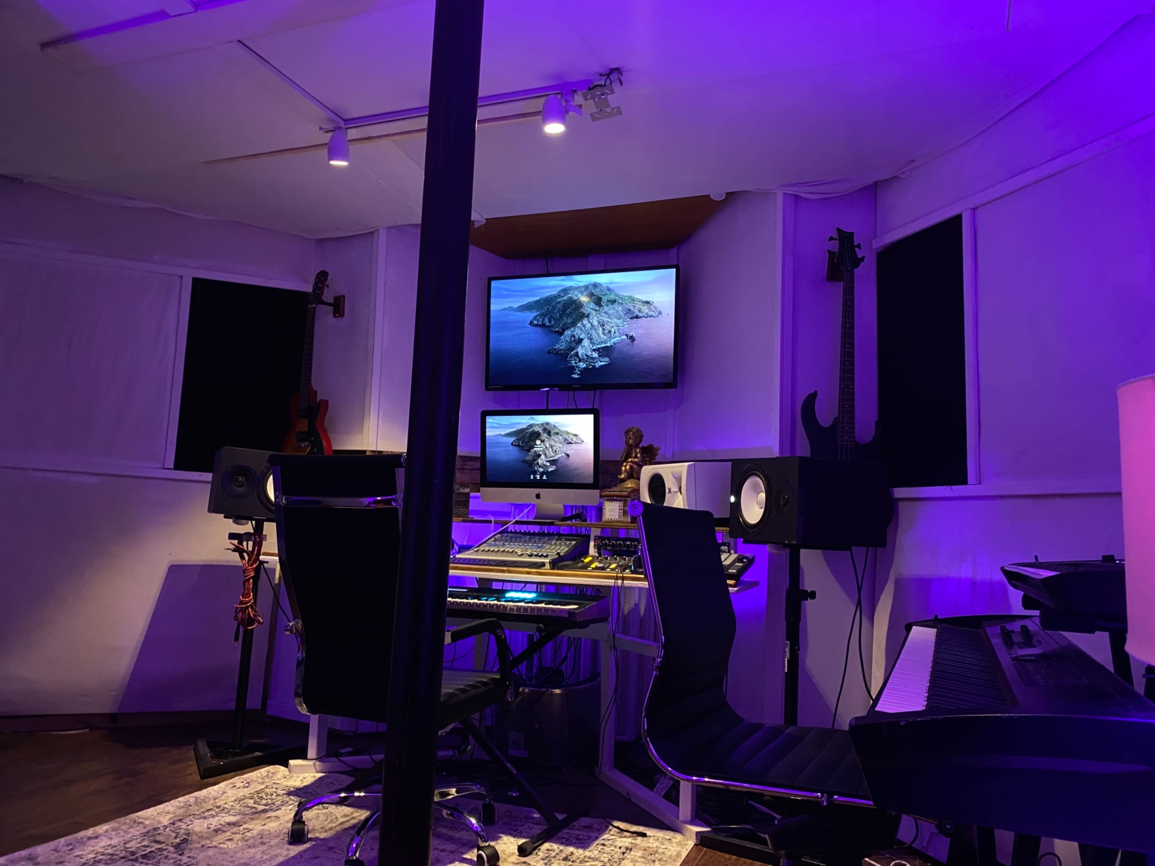 A home music studio features a digital audio workstation, monitors, and illuminated screens displaying an island view.