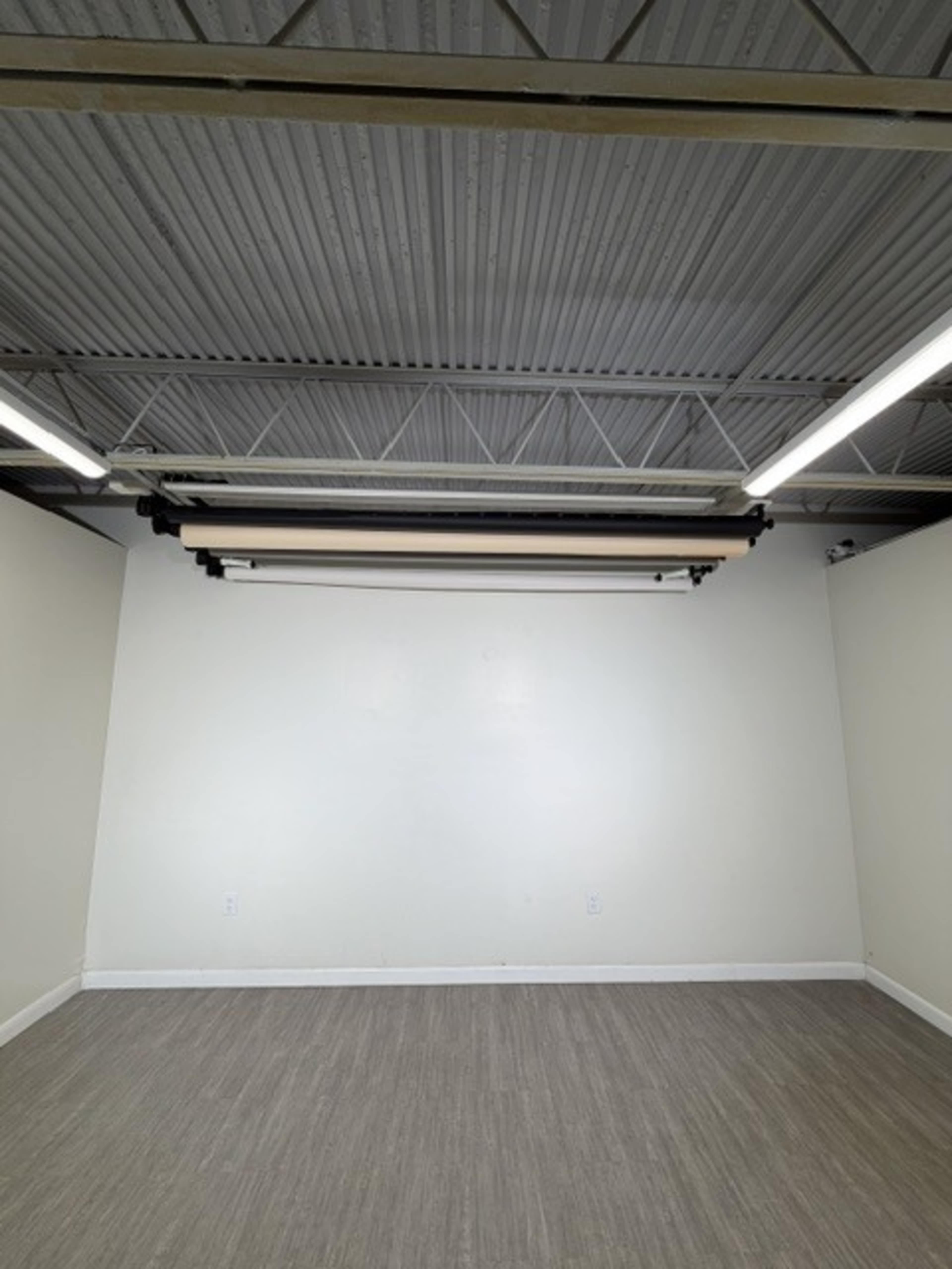 The image shows an empty room with light-colored walls, a flat gray floor, and a ceiling-mounted equipment track.