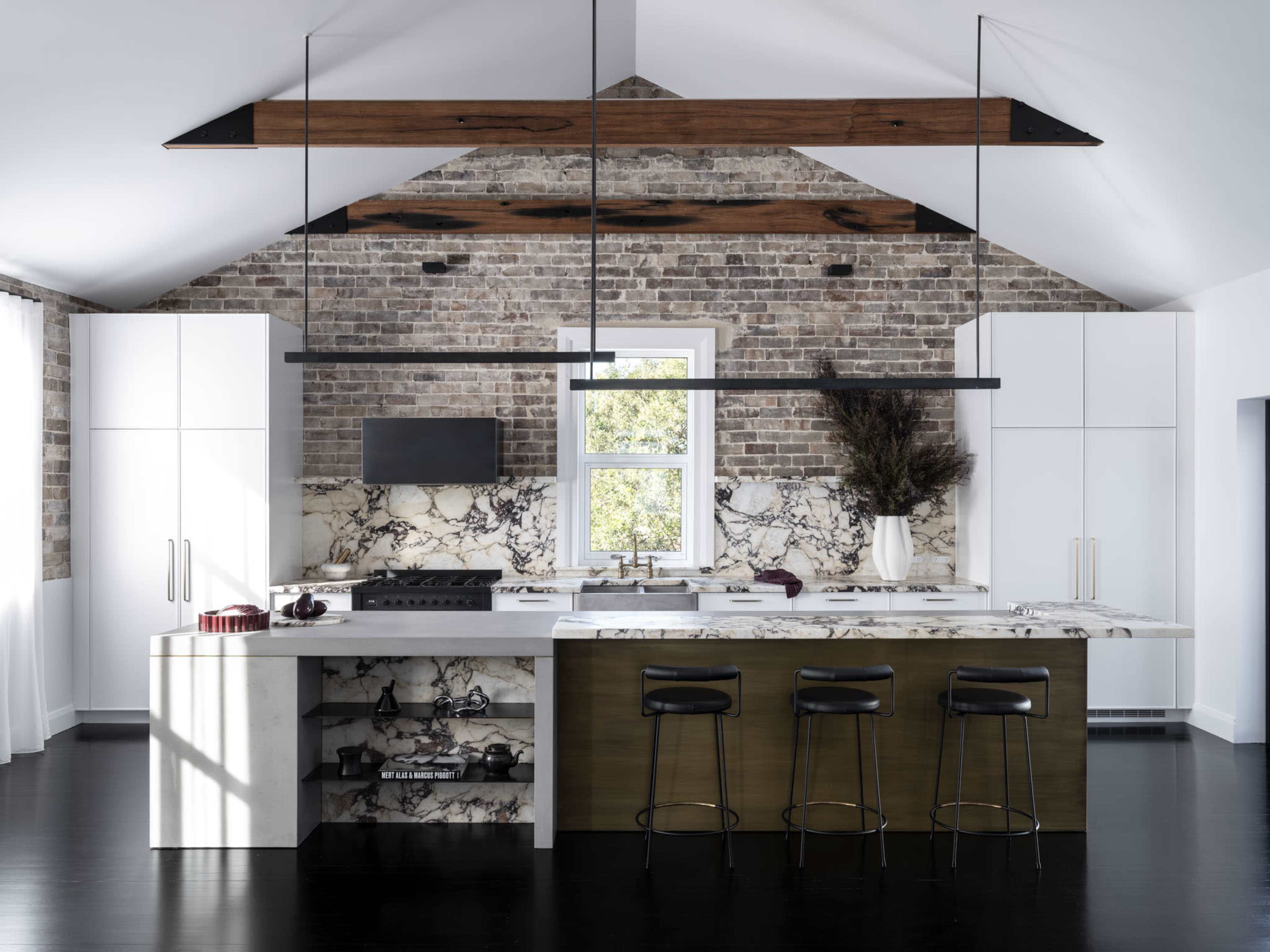 The kitchen features a mix of modern and rustic design elements, with a marble island, dark cabinetry, and exposed brick walls.