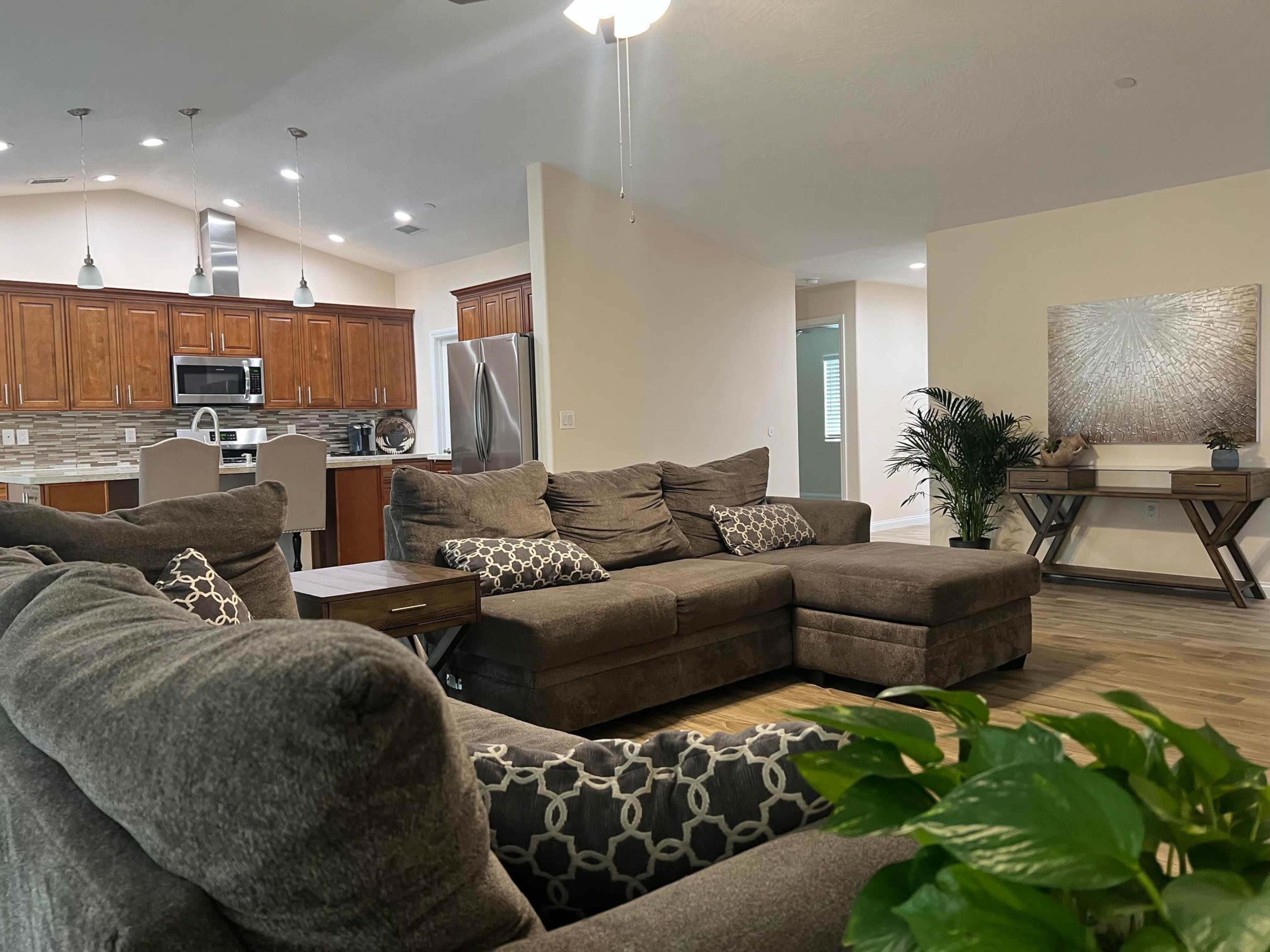 A modern living room with a large sectional sofa, a coffee table, and an open kitchen area in the background.