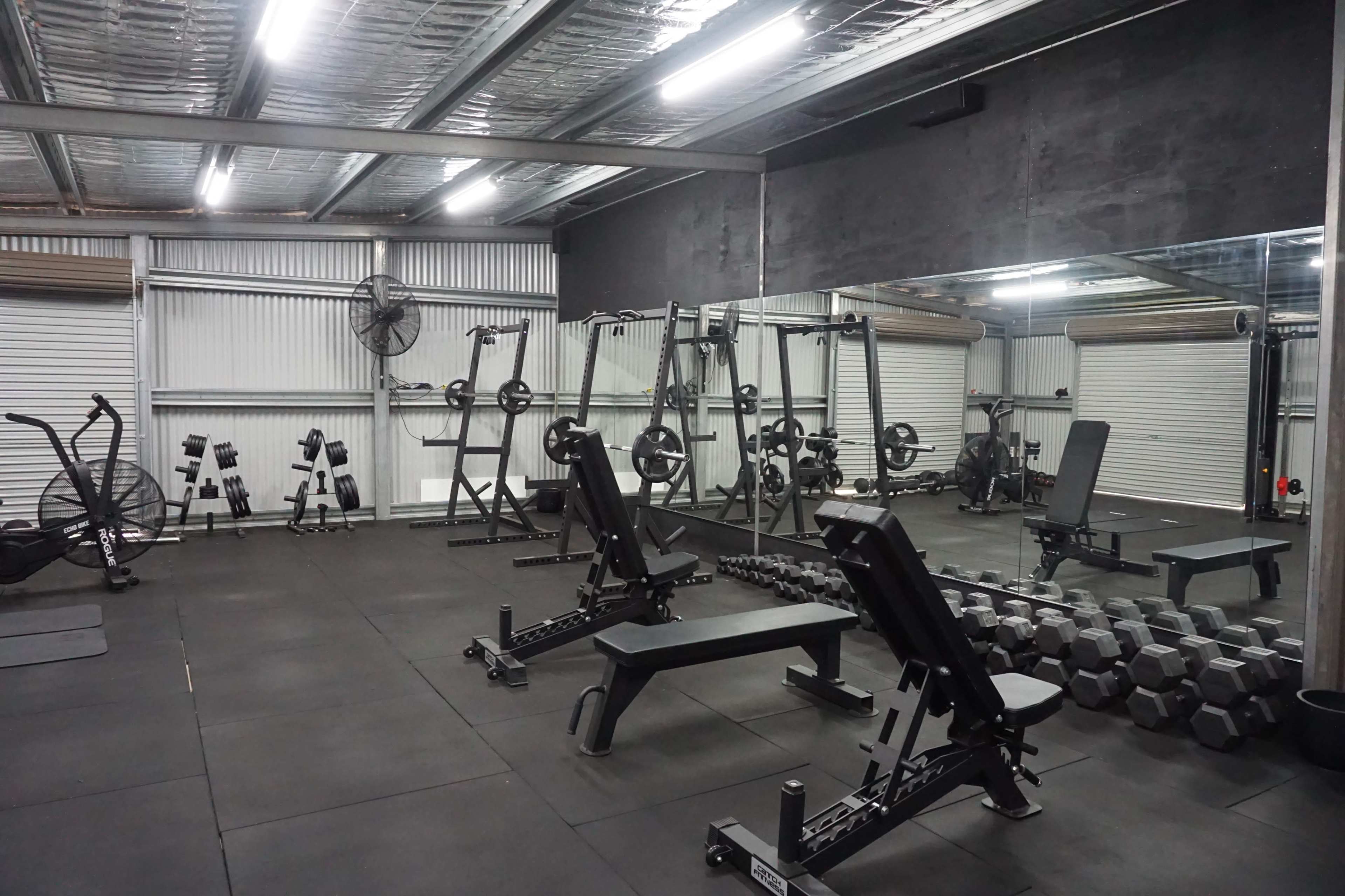 A gym area equipped with various exercise machines, weights, and benches, all arranged on a rubber floor.