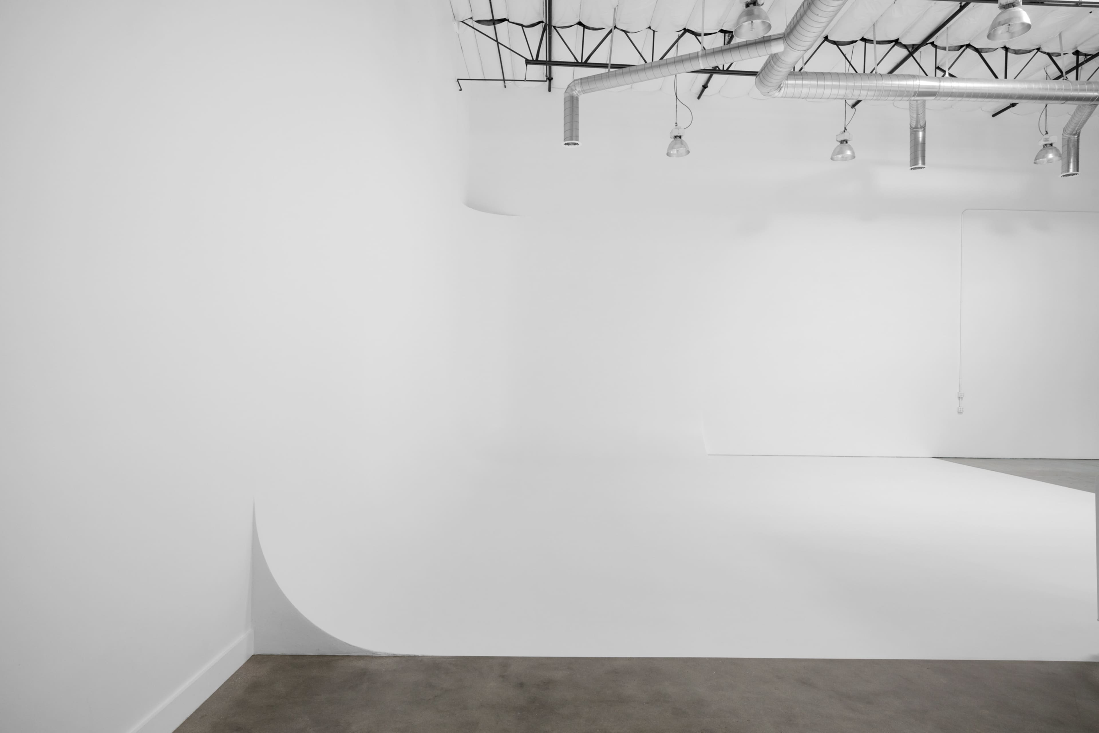 A spacious, minimalist studio with white walls, a smooth floor, and industrial lighting fixtures.