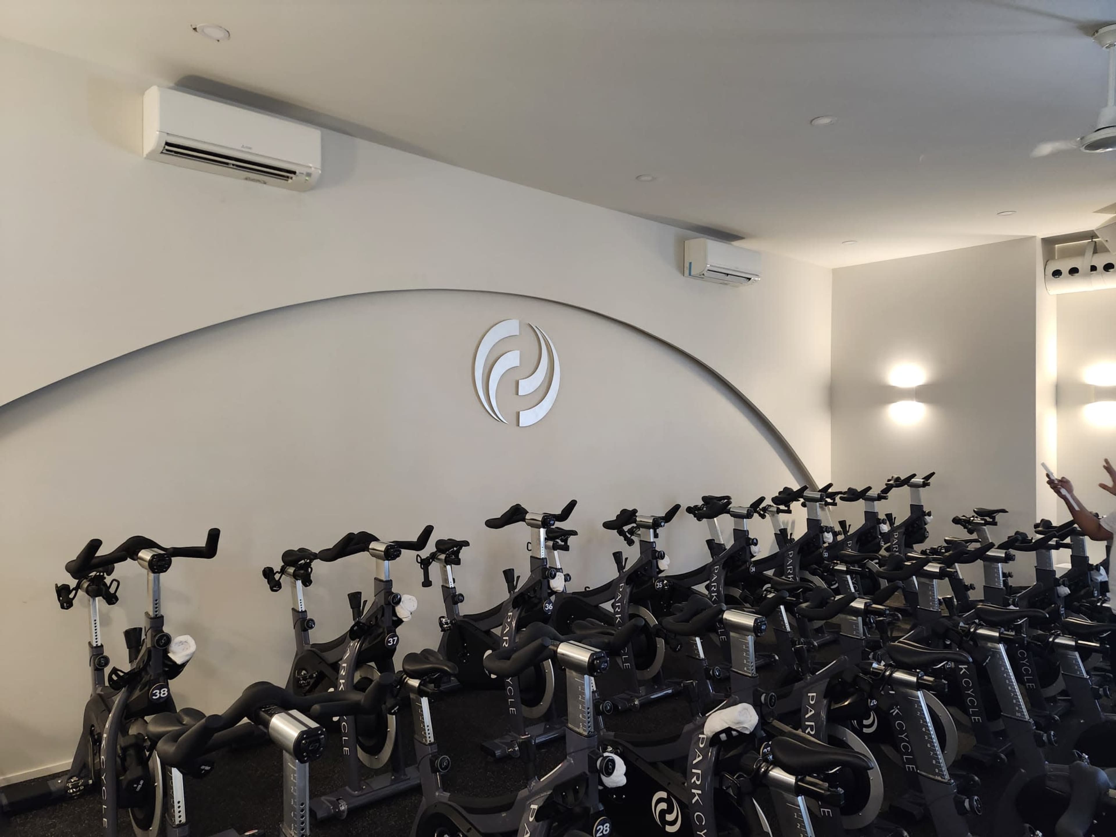 The image shows an indoor cycling studio with rows of stationary bikes facing a curved wall featuring a logo.