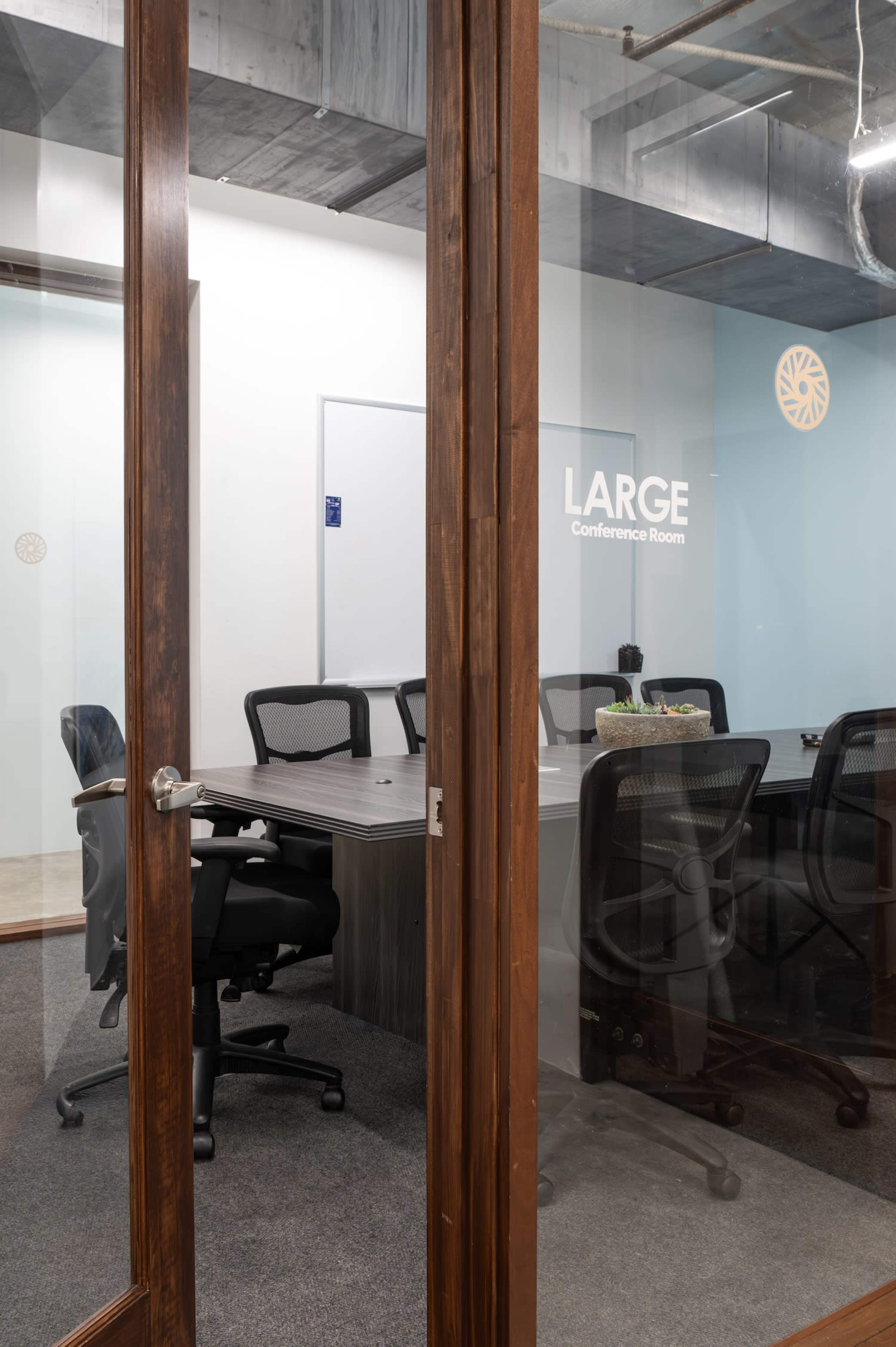 A glass door opens into a conference room with a large table surrounded by black office chairs.