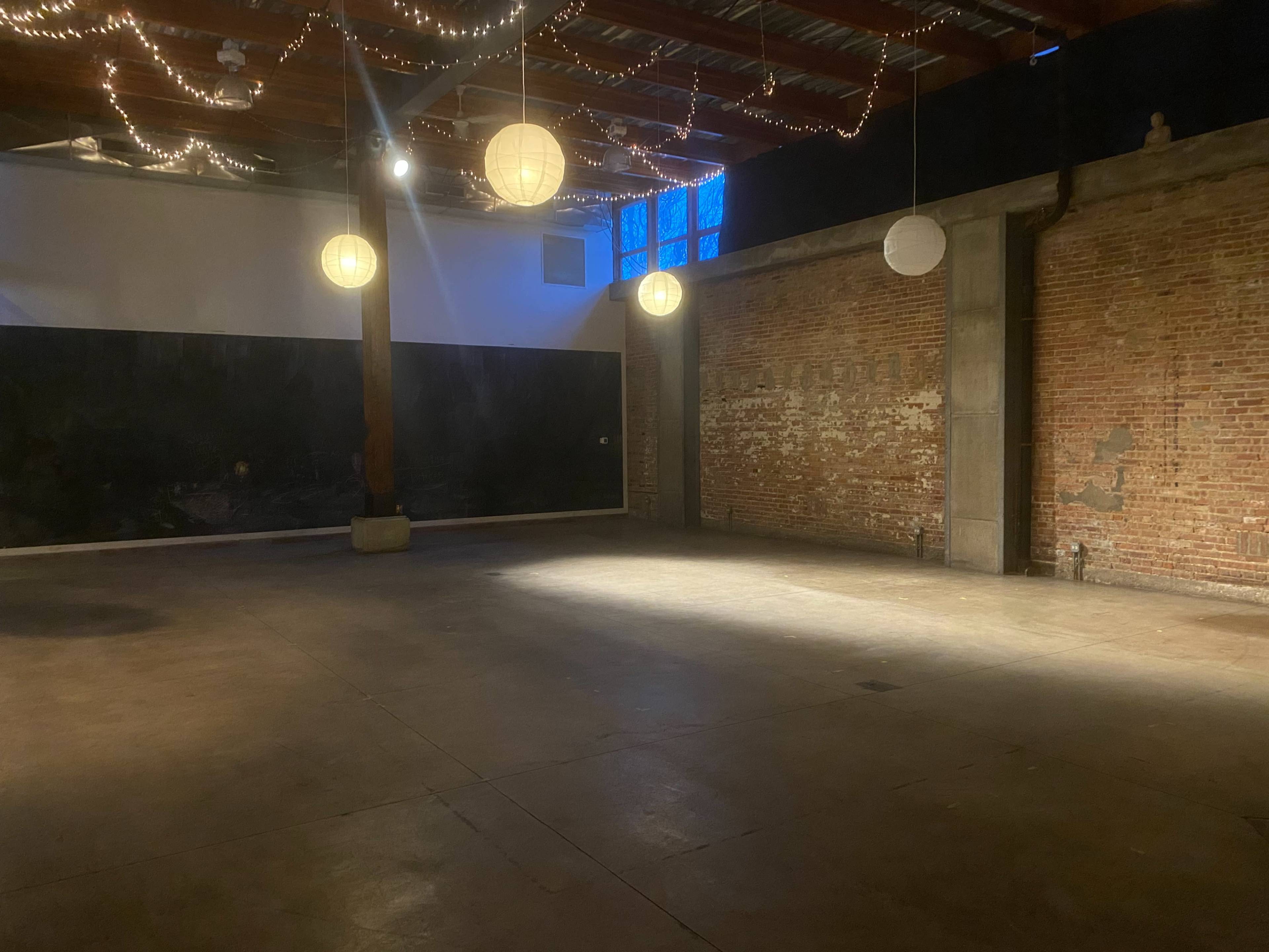 An empty interior space with exposed brick walls, a wooden ceiling, and decorative paper lanterns hanging above.