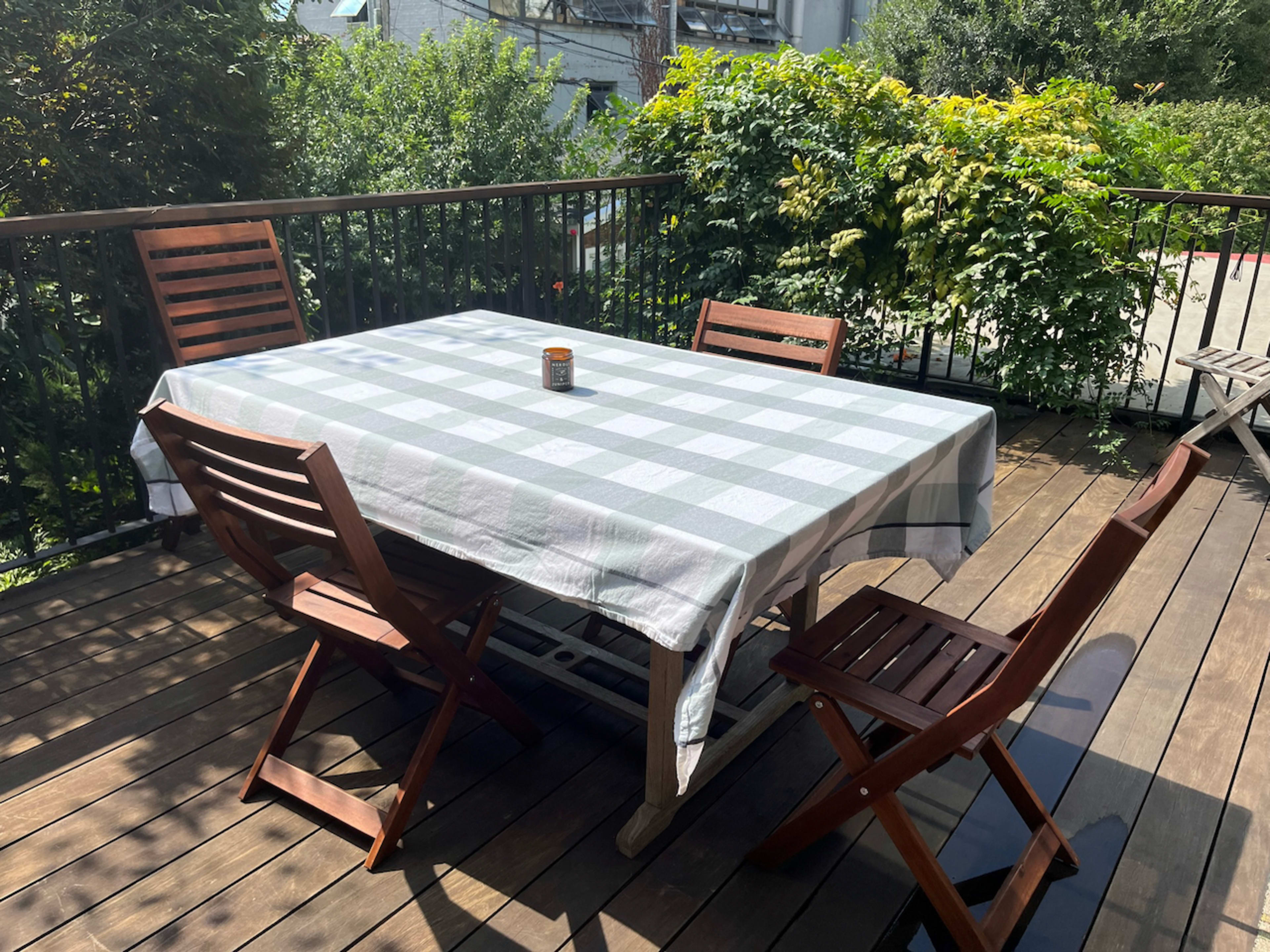 A wooden deck features a rectangular table with a checkered tablecloth surrounded by four wooden chairs.