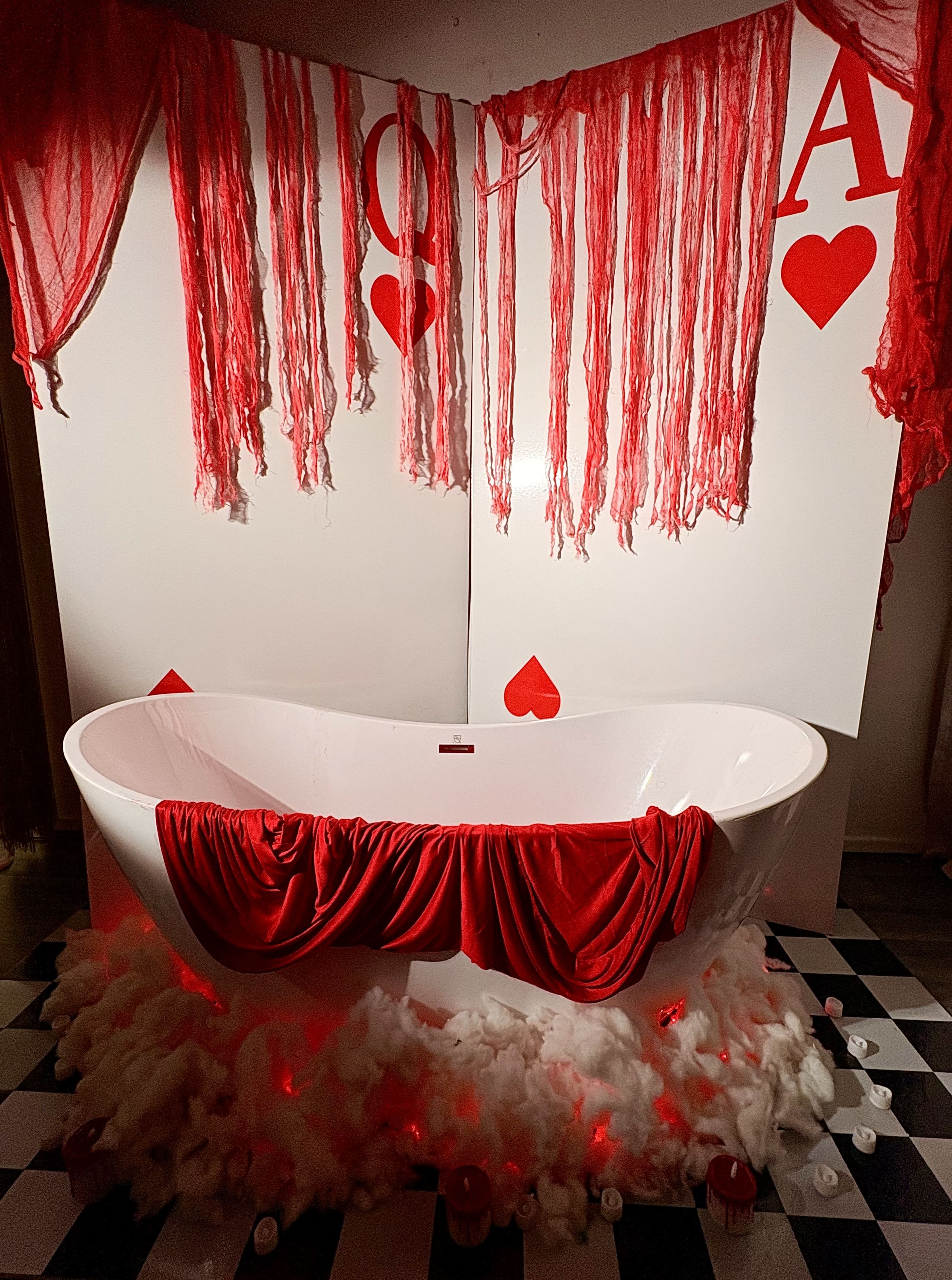 The scene features a white bathtub draped with red fabric, surrounded by a cloud-like material on a black and white checkered floor, with red and white decorations on the walls.