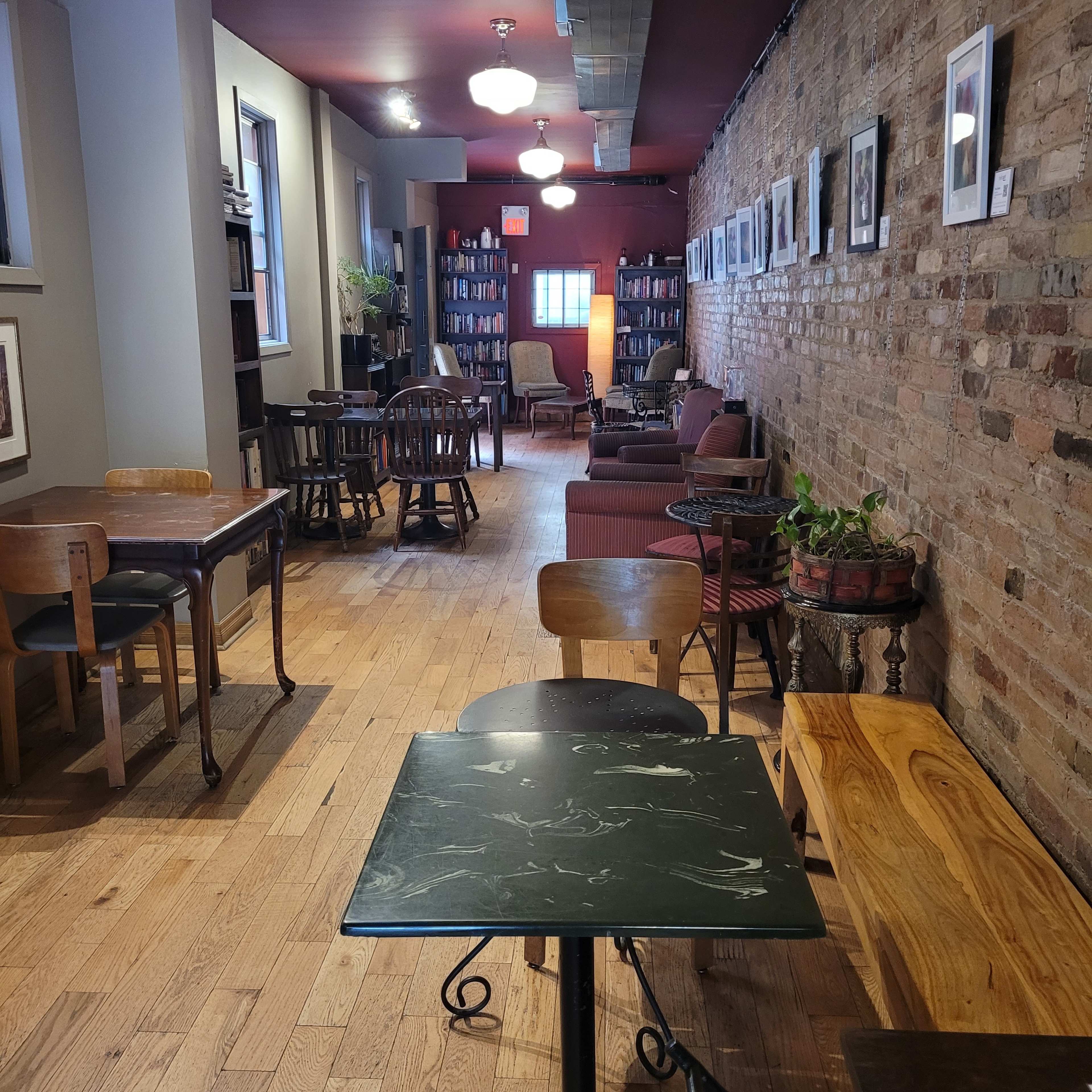 A cozy café interior with wooden floors, exposed brick walls, and various seating arrangements along a well-lit corridor.