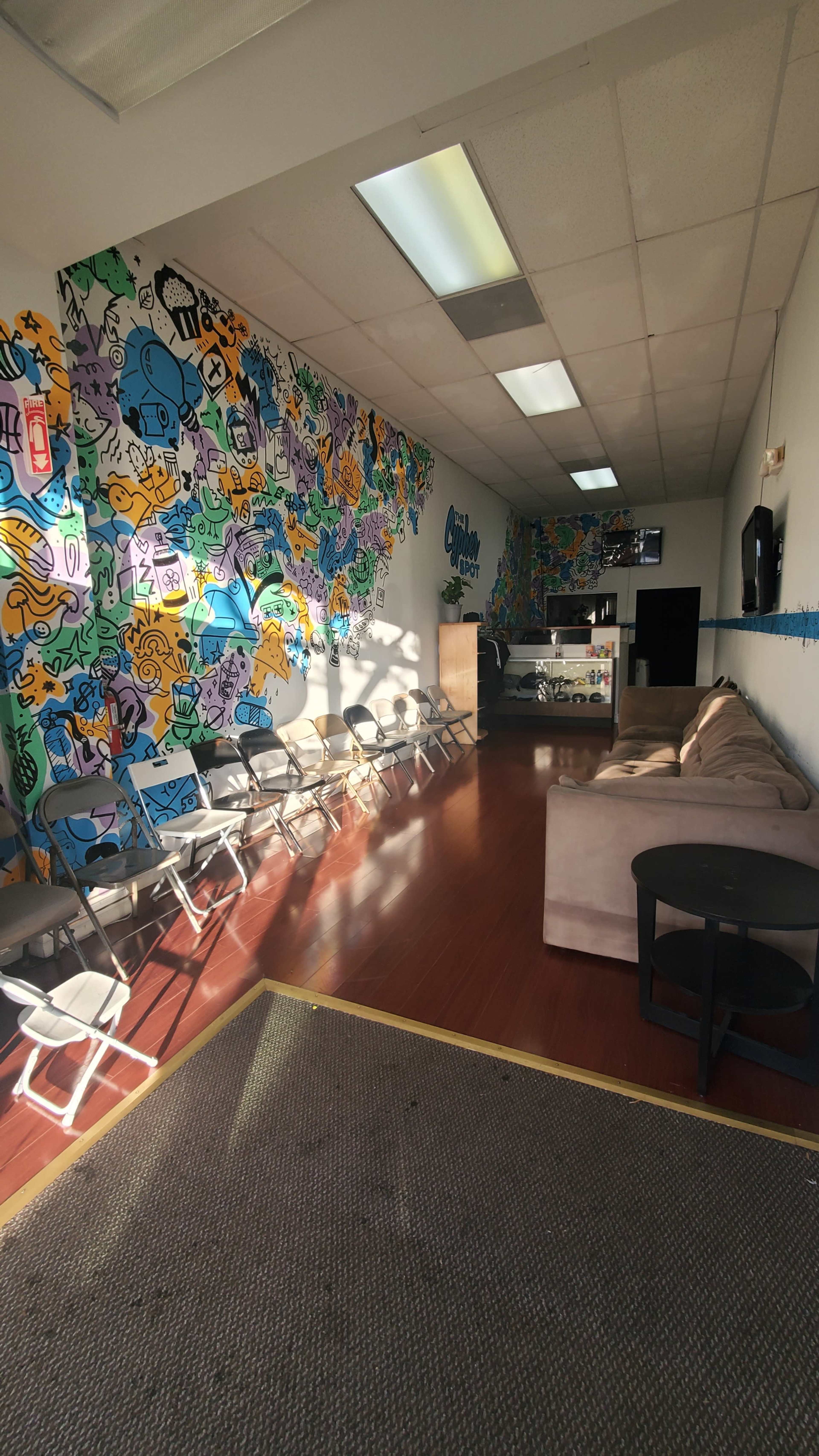 A brightly colored, mural-adorned interior of a modern lounge with a couch, folding chairs, and a reception area.