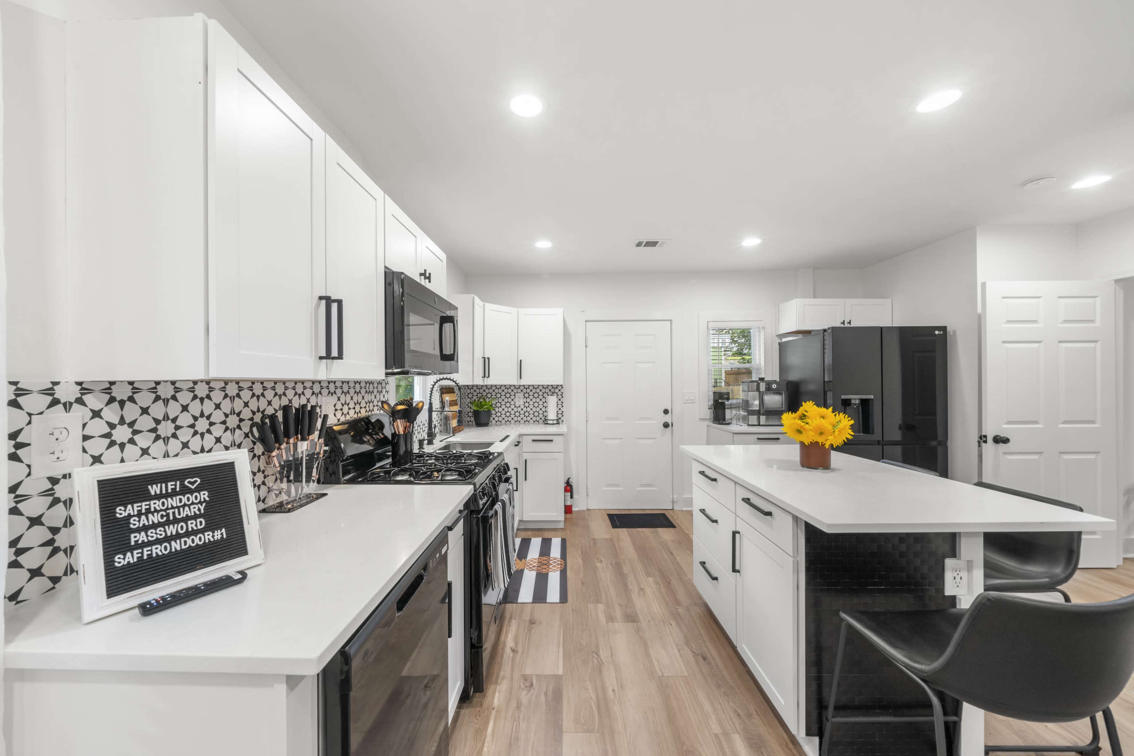 A modern kitchen with white cabinets, black appliances, and a patterned backsplash, featuring a central island and a door leading outside.