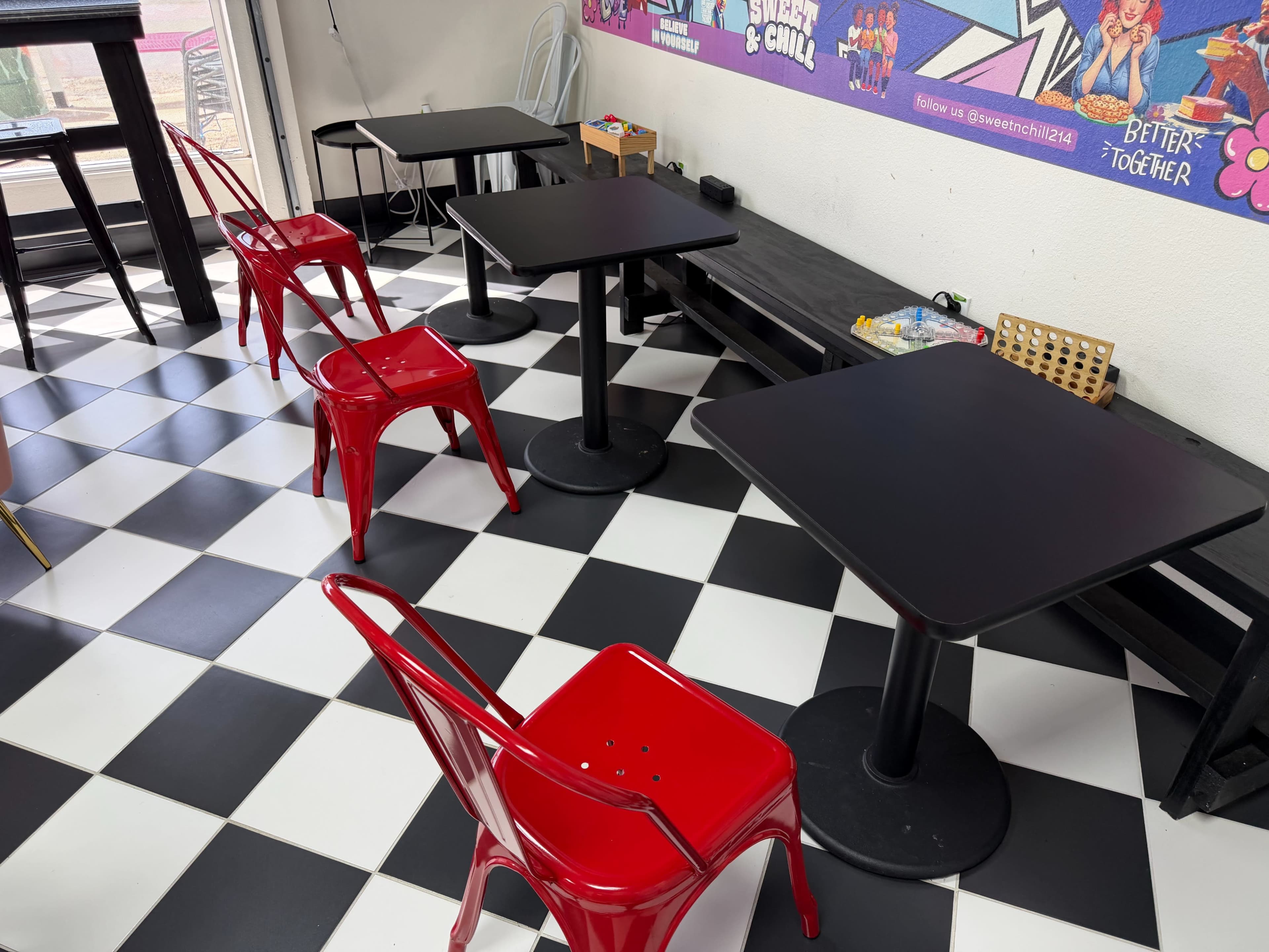 The image shows a seating area with red metal chairs and black tables arranged on a black and white checkered floor.