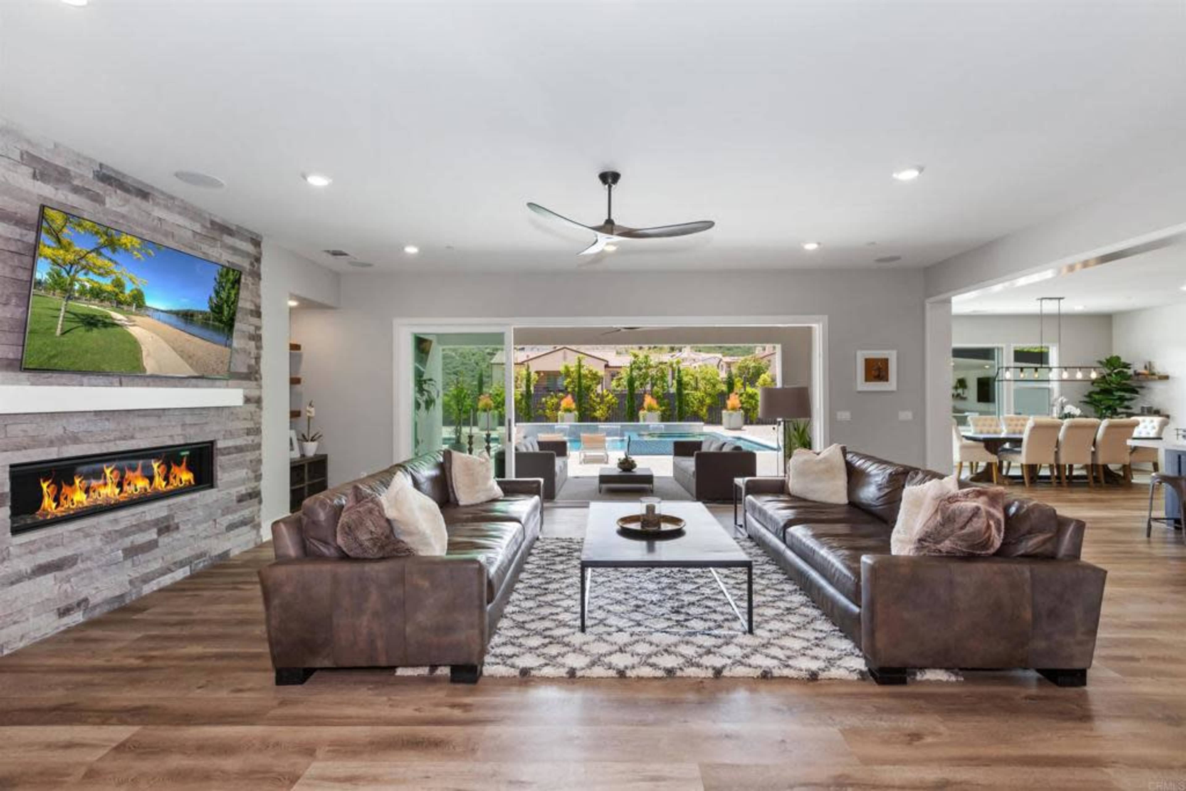 The living room features two leather sofas facing each other with a fireplace and large windows overlooking an outdoor pool area.