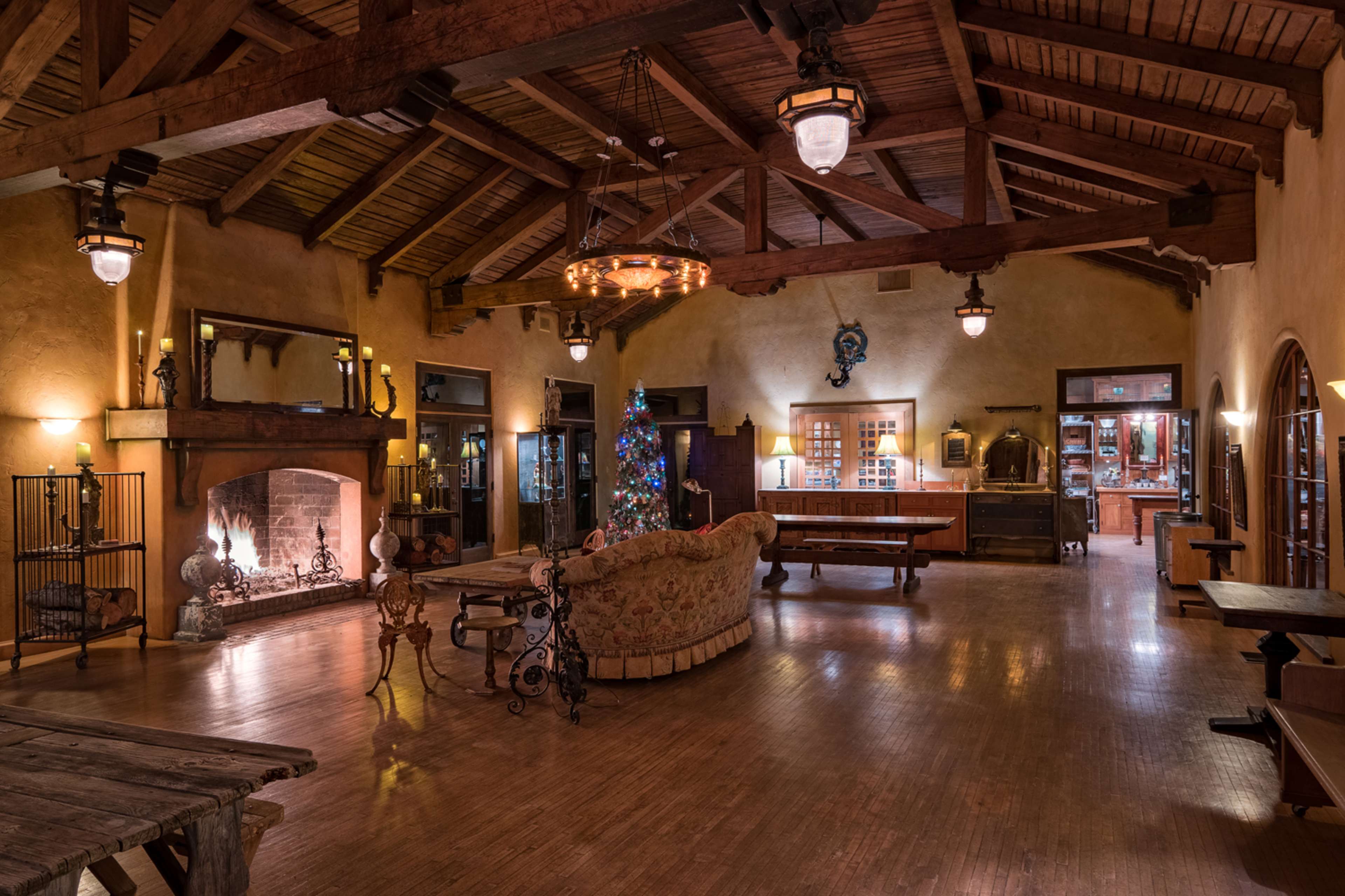 A spacious interior of a rustic lodge, featuring a large fireplace, wooden beams, and a decorated Christmas tree.