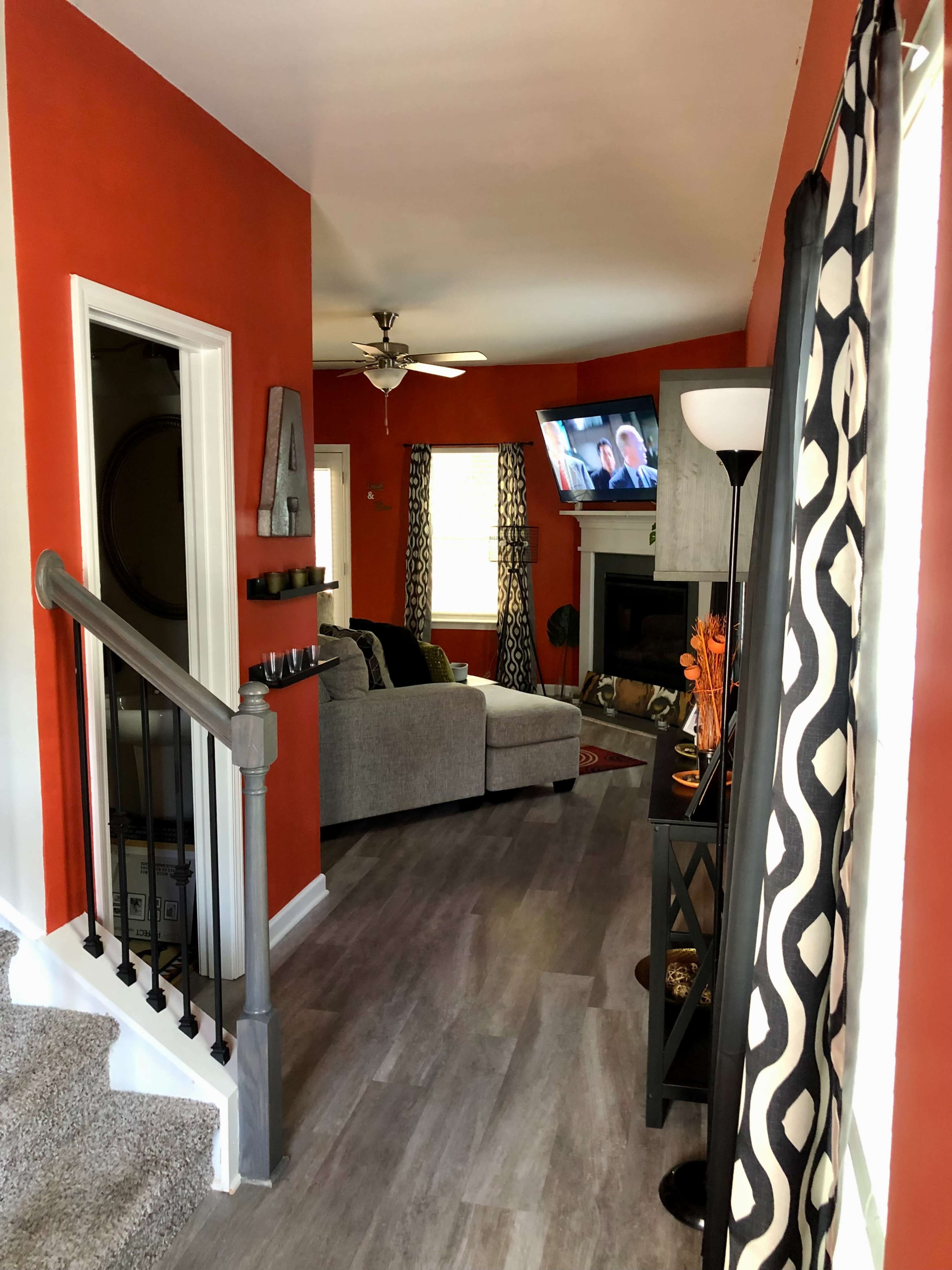 A living area with an orange wall, a gray couch facing a television, and a staircase leading to another level.