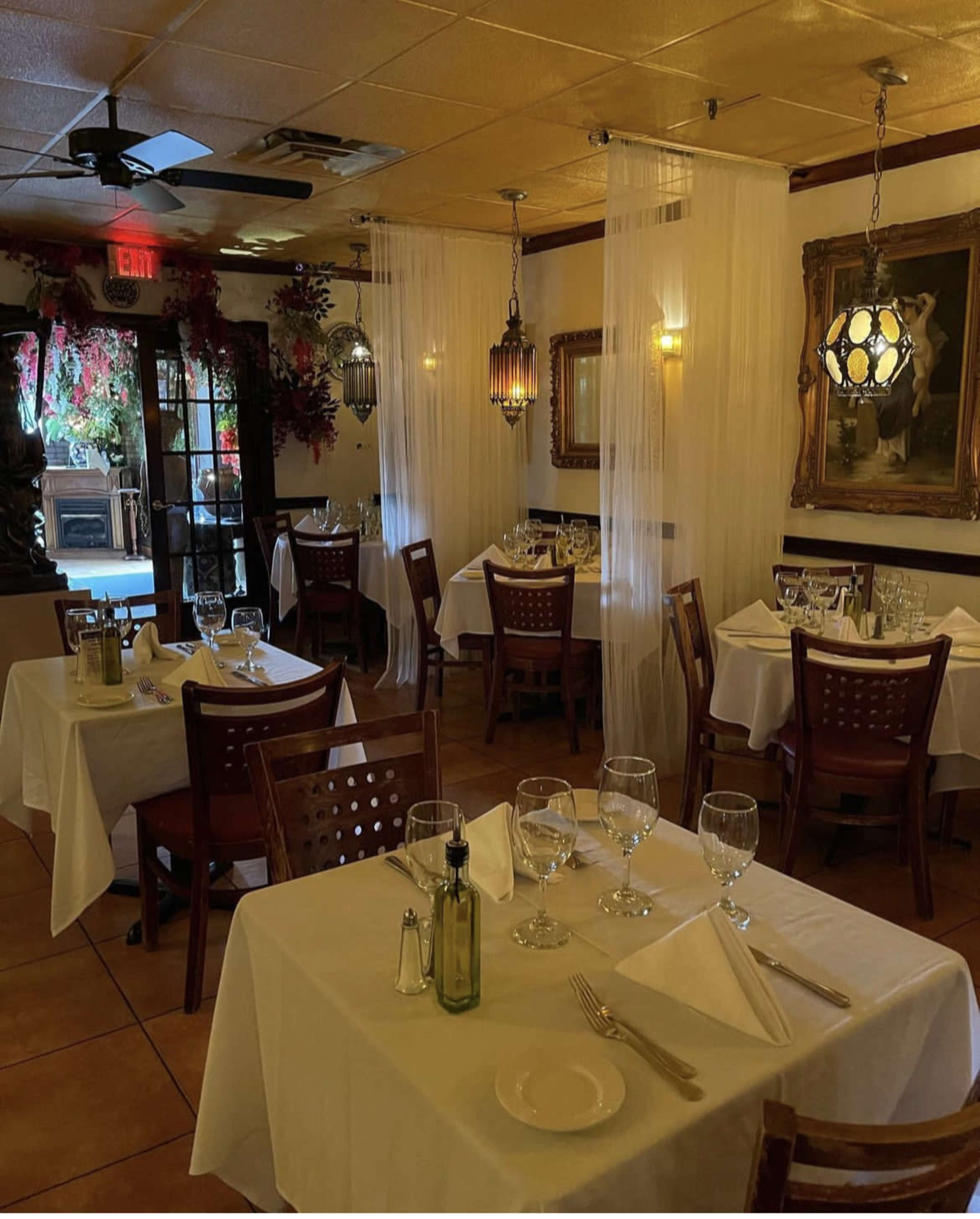 A dining area in a restaurant with tables neatly covered in white cloths, accompanied by glassware and dim lighting from decorative fixtures.