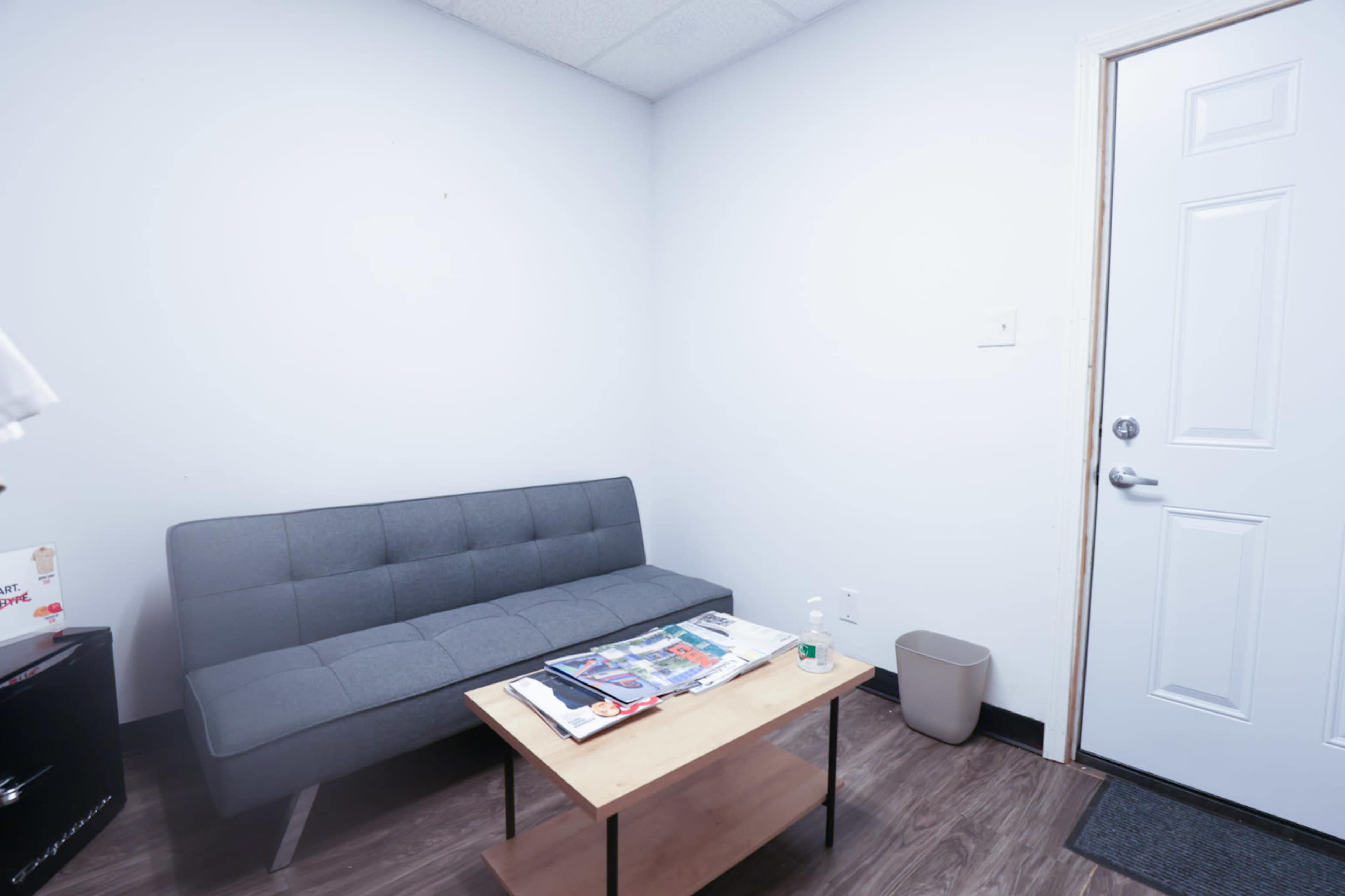 A small waiting room with a gray sofa, a wooden coffee table with magazines, and a door leading outside.