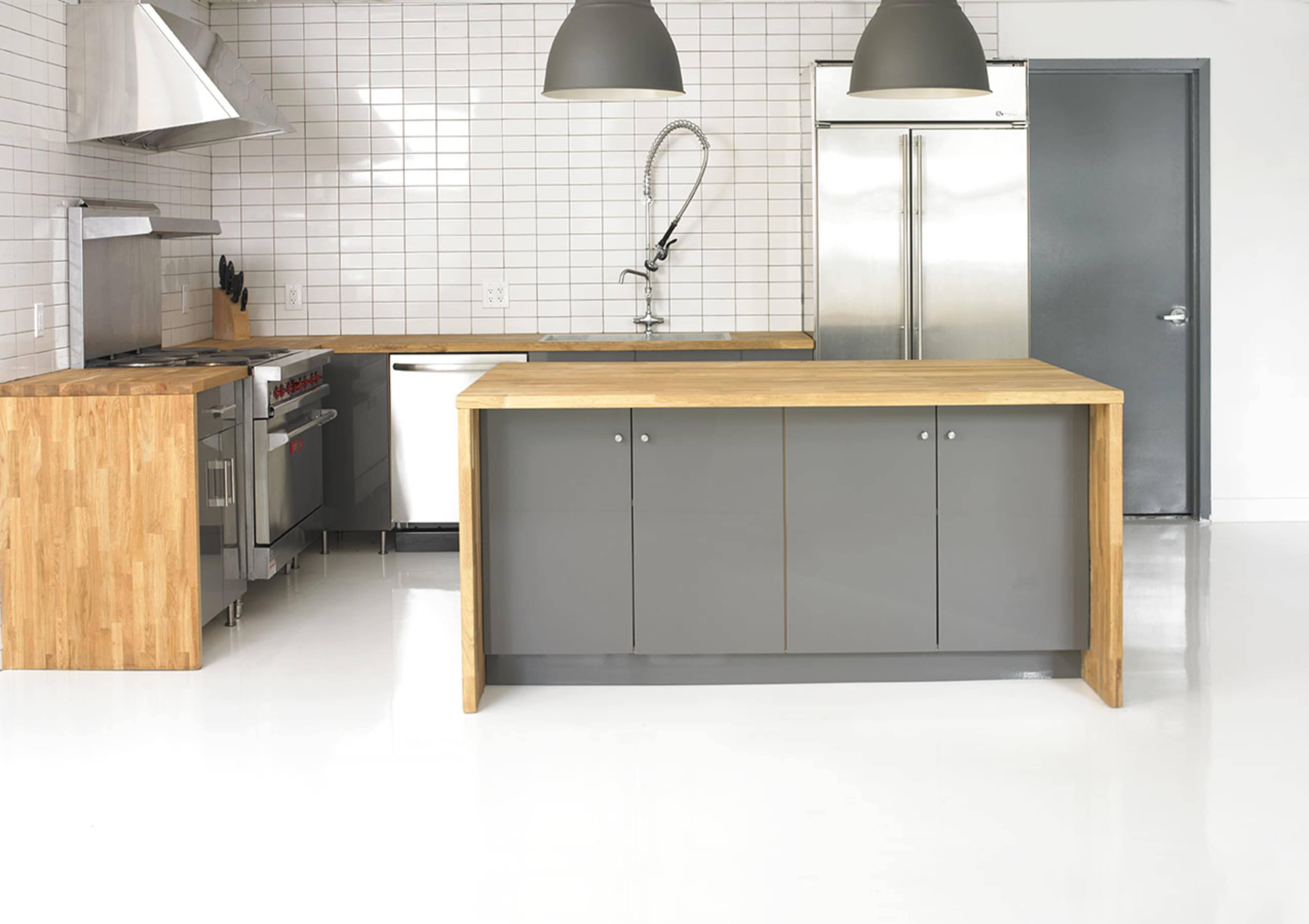 A modern kitchen features a stainless steel range, a wood-topped island, and gray cabinetry against a tiled wall.