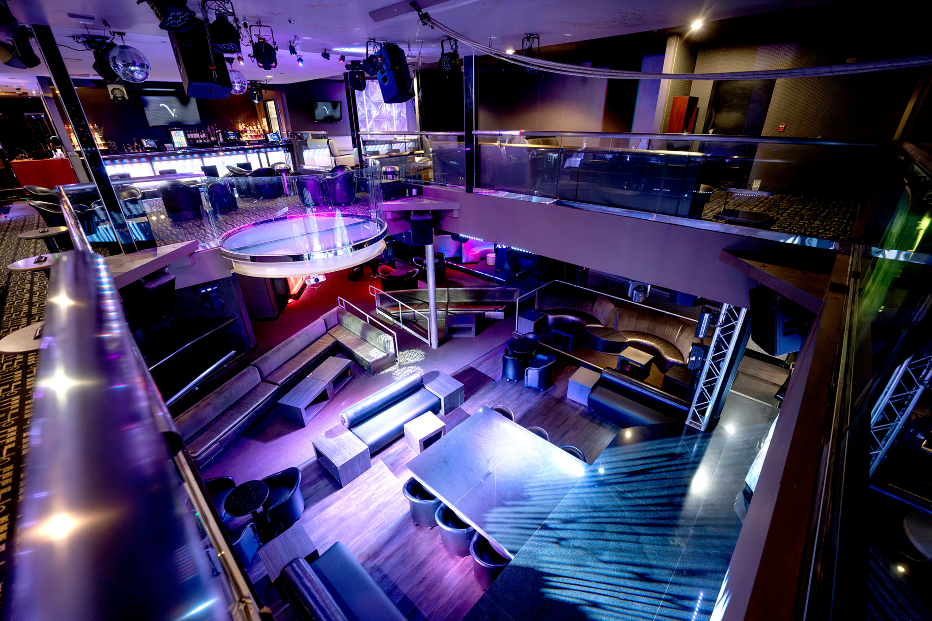 The image shows a modern nightclub interior with multi-level seating, vibrant lighting, and a bar area.