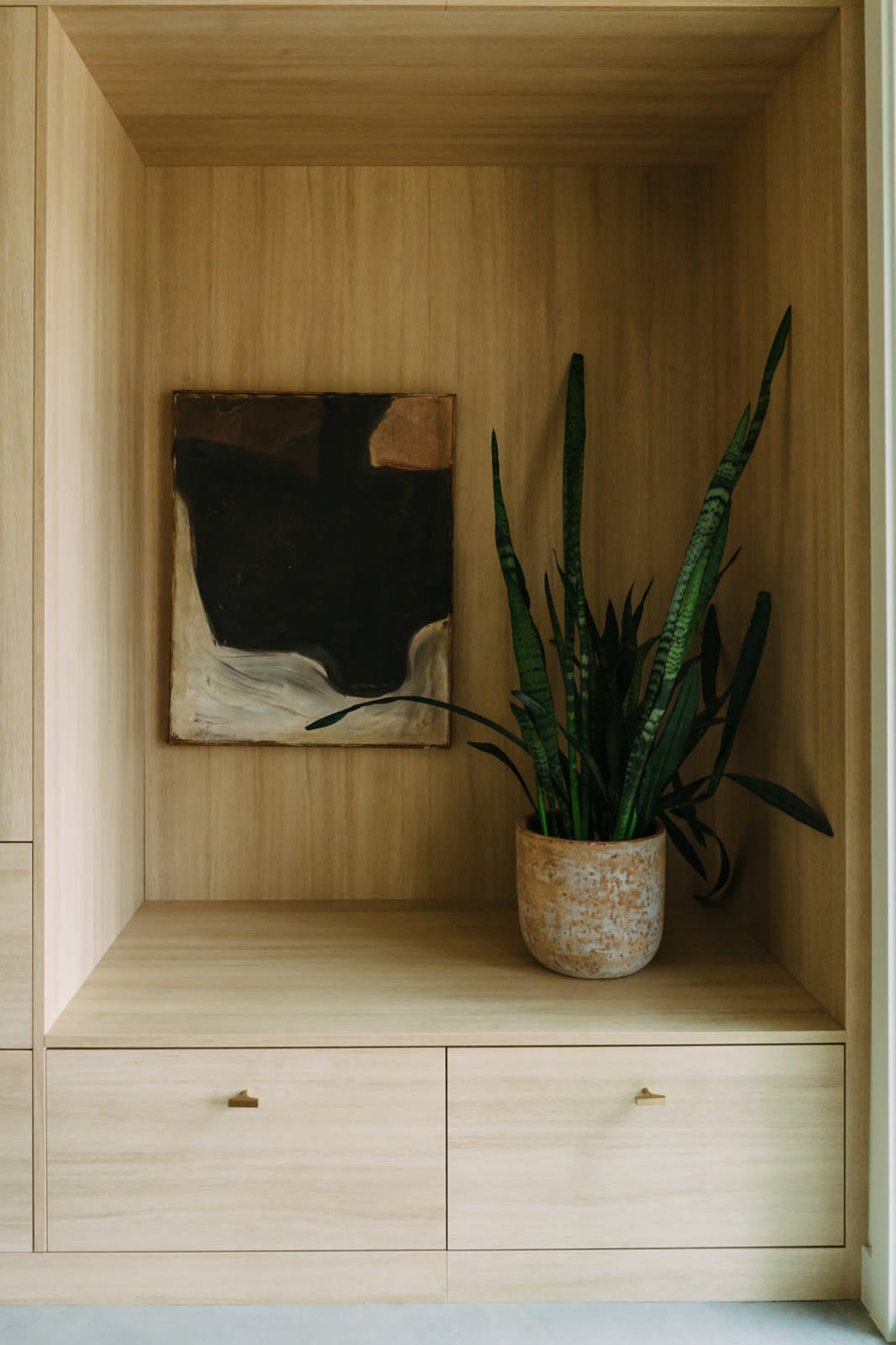 A wooden shelf features an abstract painting and a potted snake plant.