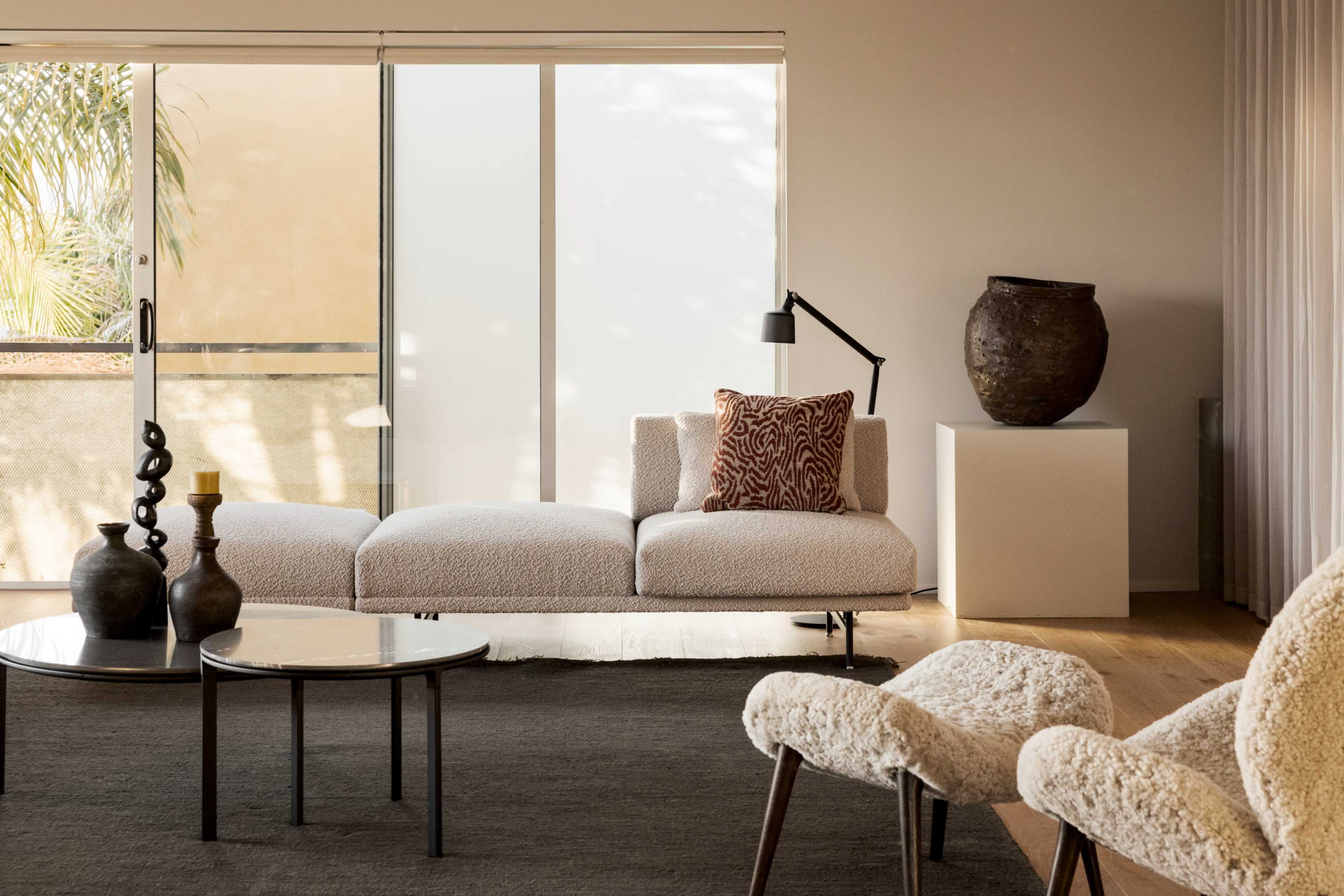 A modern living room features a plush, U-shaped sofa with a decorative pillow, accompanied by a round coffee table and stylish chairs, all set against large sliding glass doors and a textured rug.
