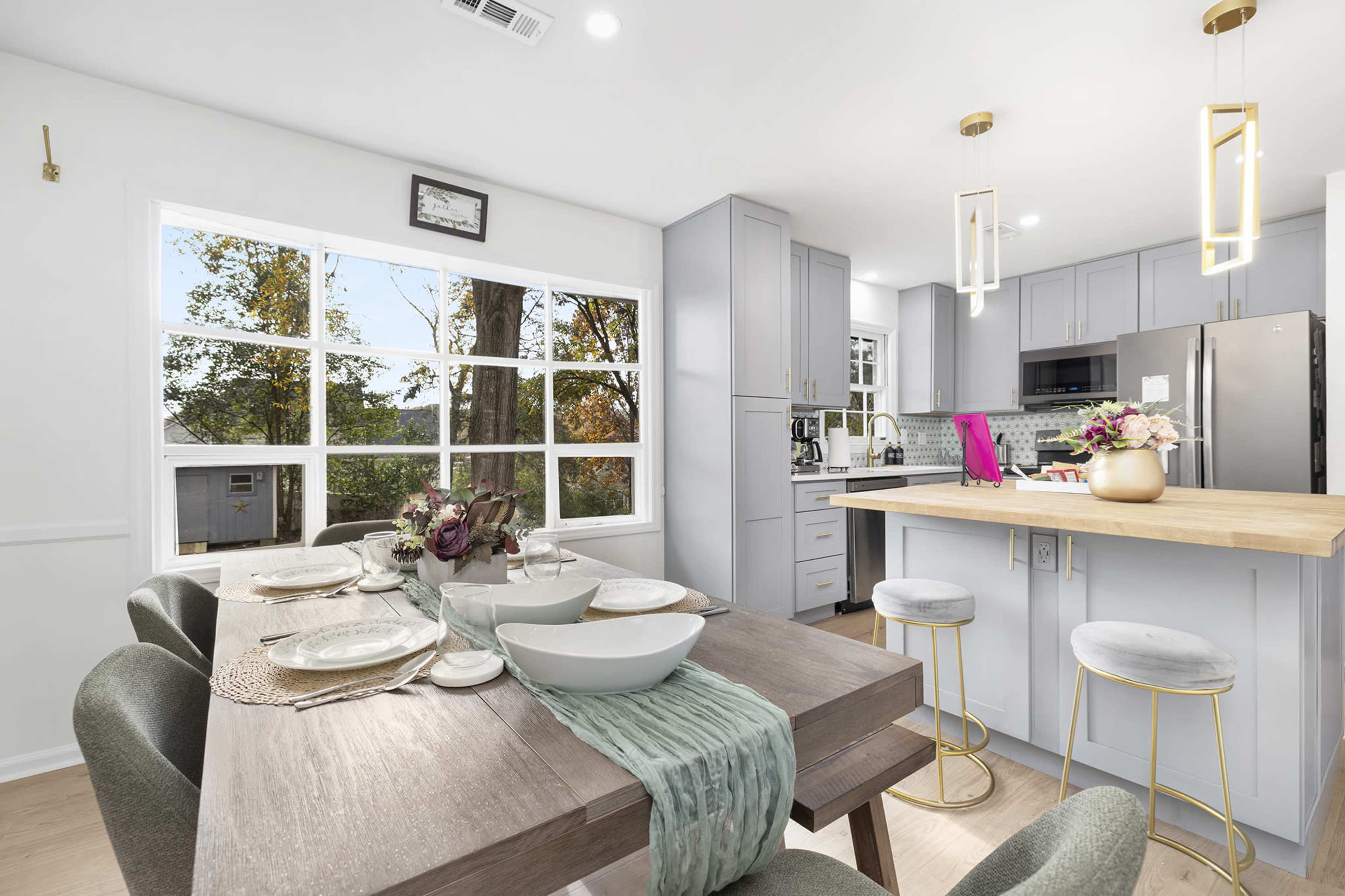 A modern kitchen and dining area feature a wooden table set for dinner, with a light-colored island and stainless steel appliances in the background.
