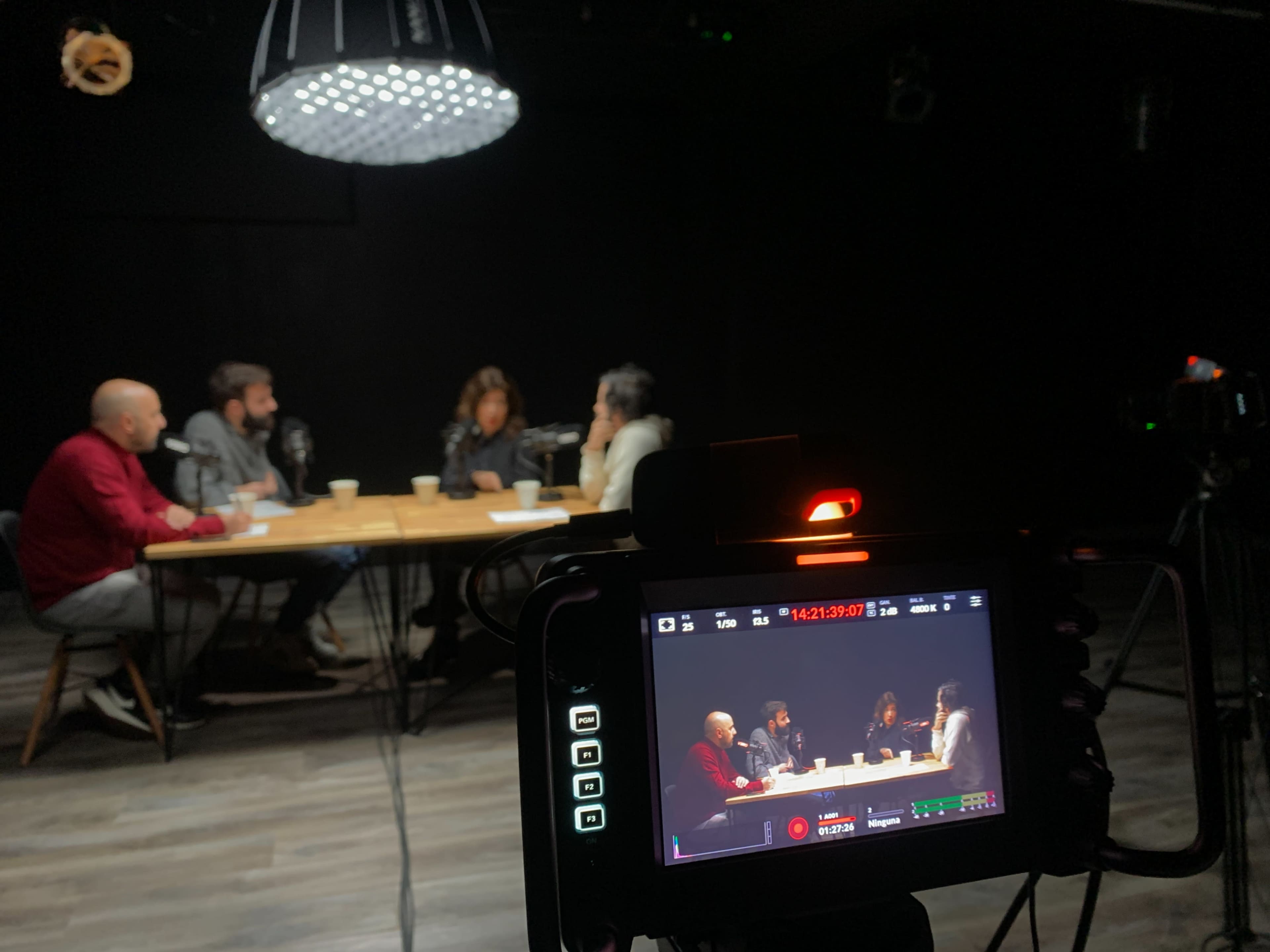 A group of six people is engaged in a discussion around a table in a dimly lit studio.