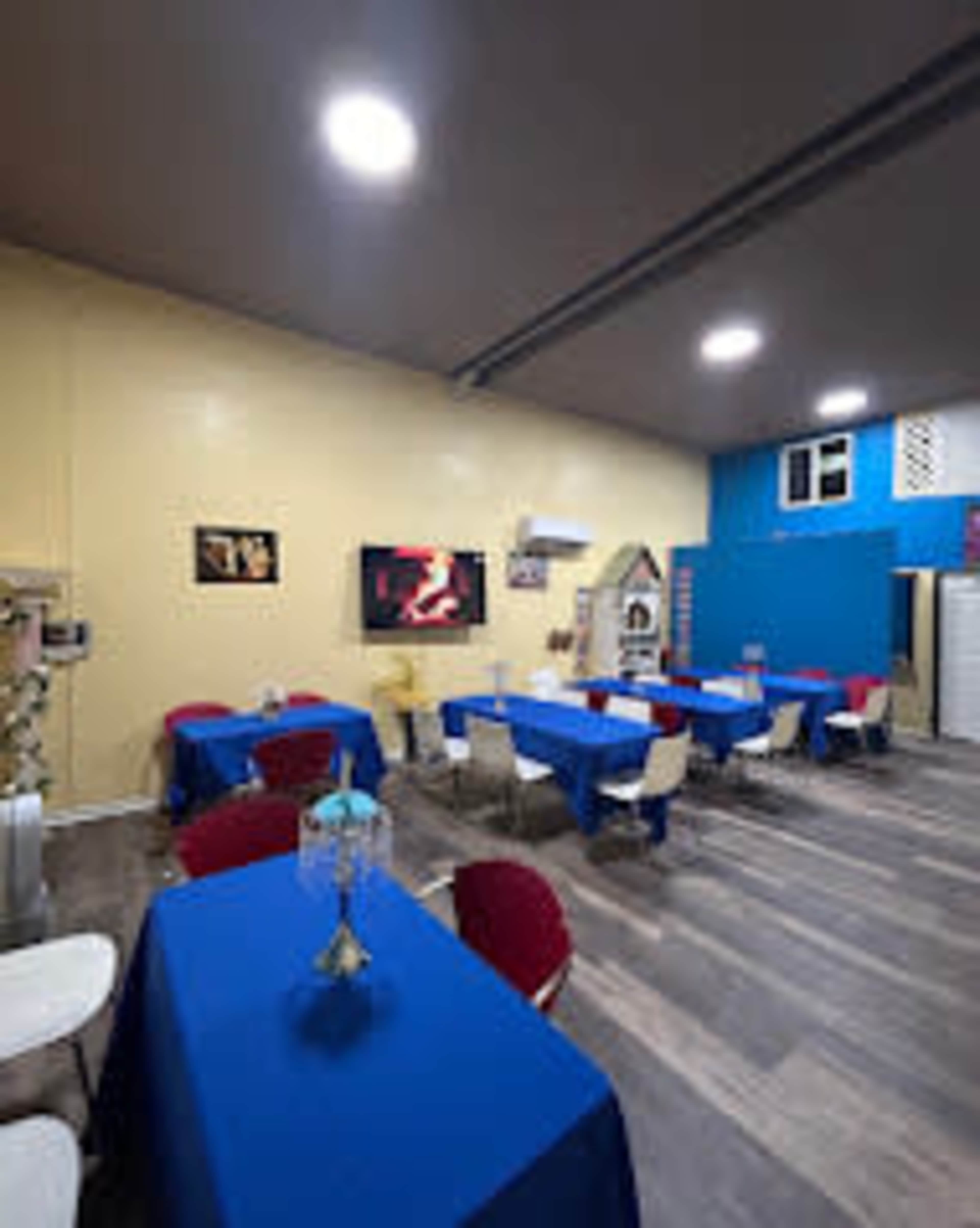 The image shows a dining area with blue and red tablecloths covering several tables, a television on the wall, and a mix of chair styles.