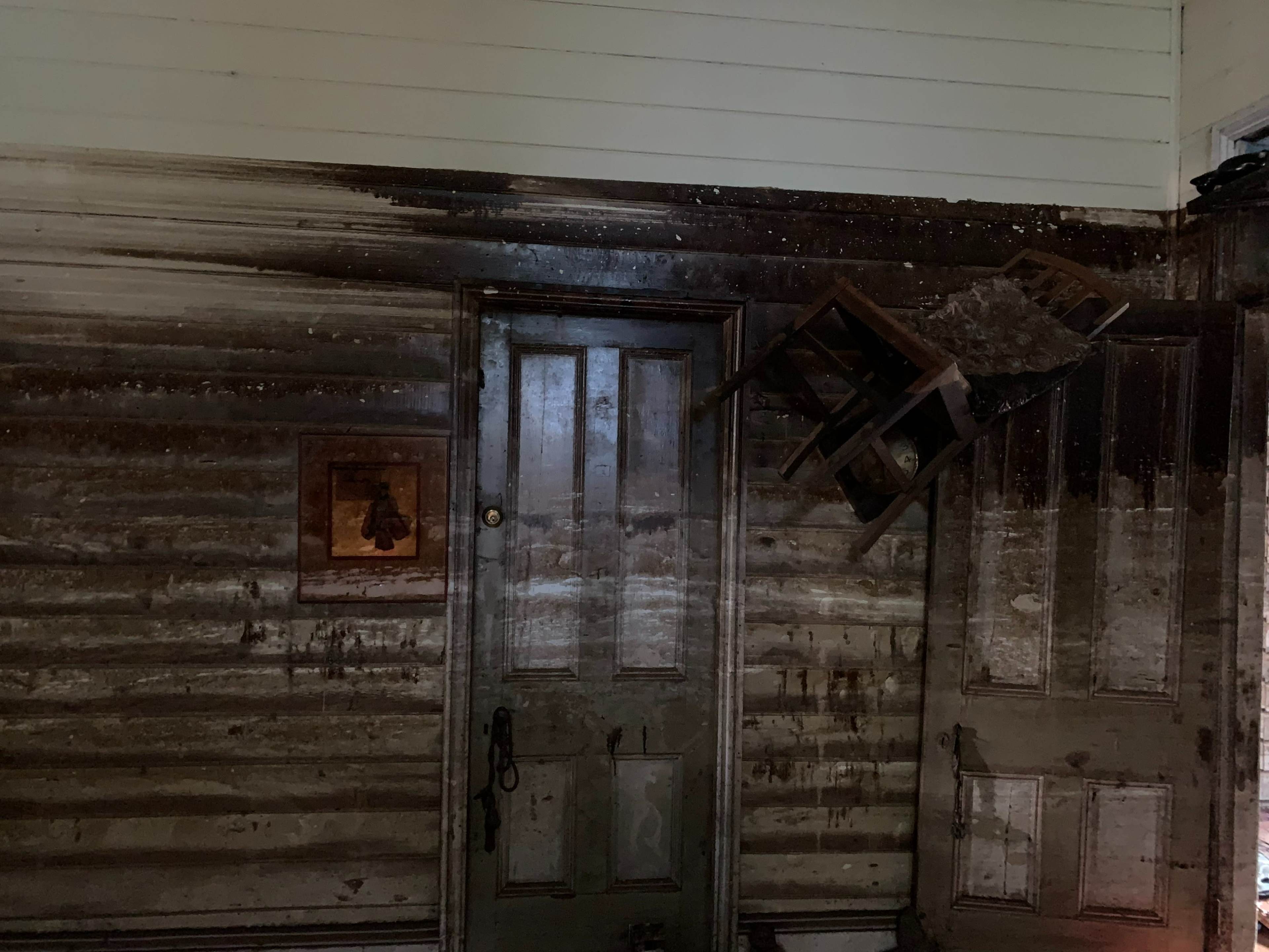 A charred wall features a door and an overturned chair, indicating recent fire damage in the room.