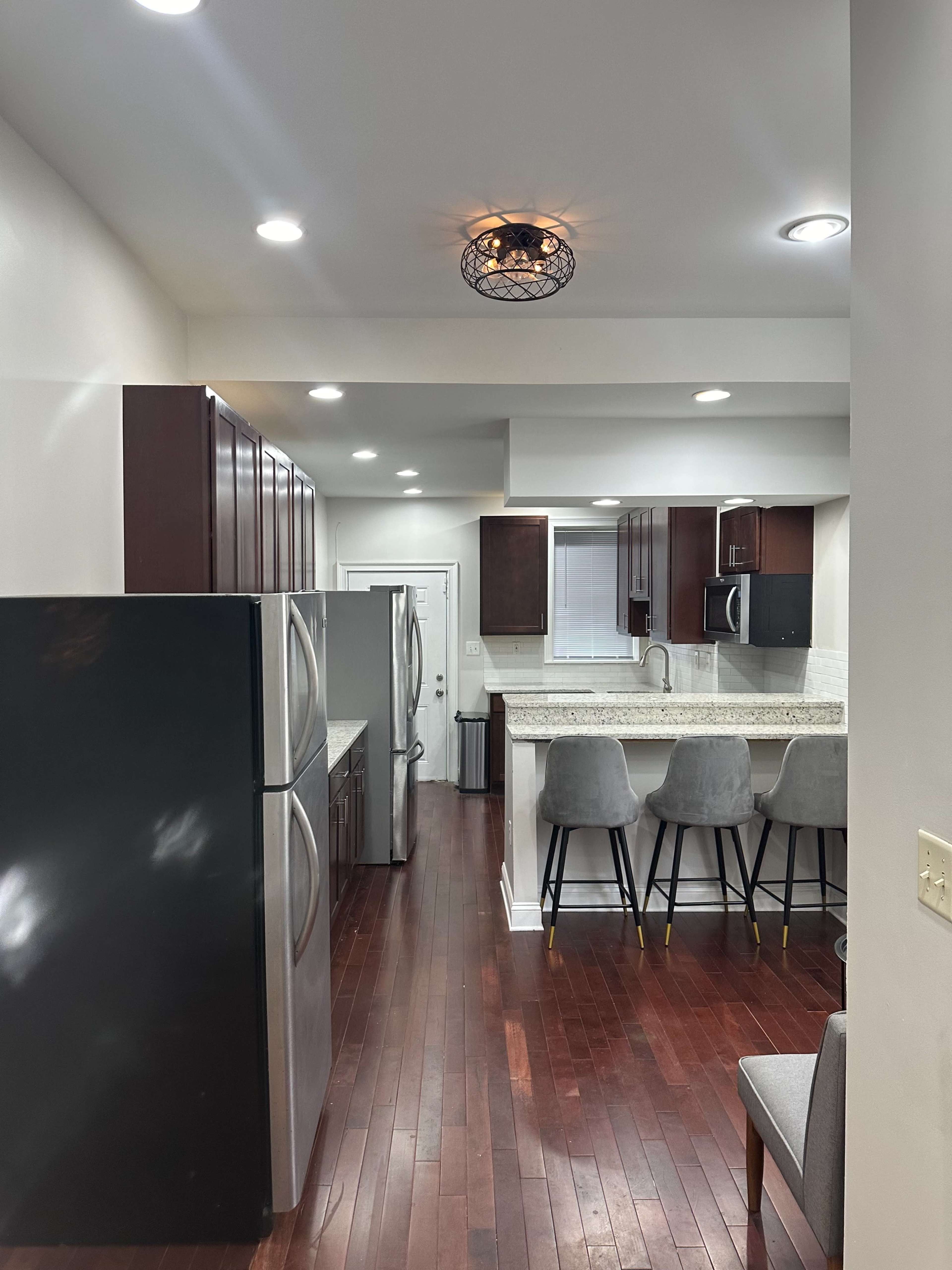 A modern kitchen with dark wood cabinets, stainless steel appliances, and a breakfast bar with gray stools.