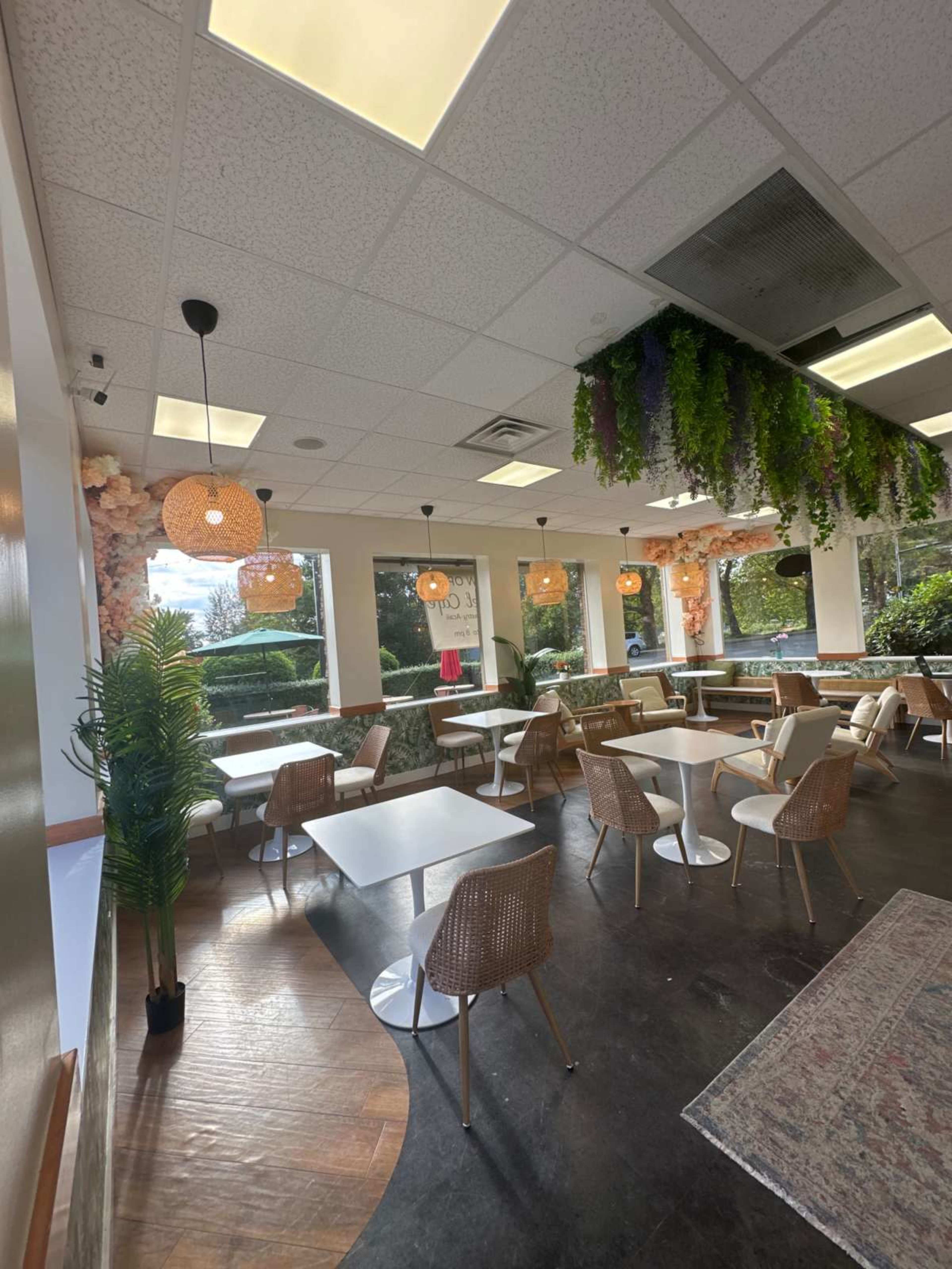 The image shows a modern café interior featuring light wood furniture, hanging pendant lights, and greenery decor.