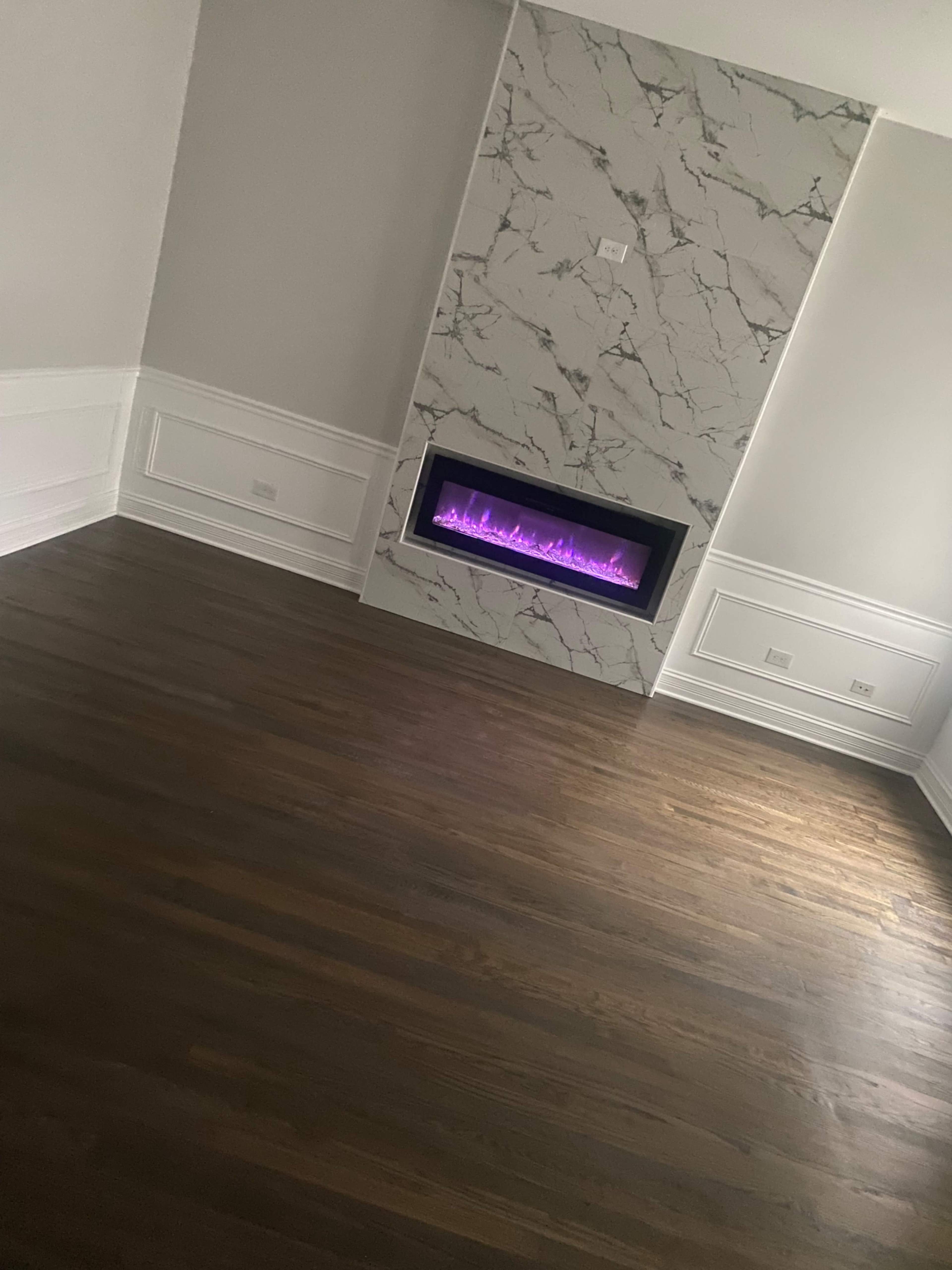 The image shows a modern living room with a marble-accented fireplace featuring purple lighting, set against dark hardwood floors.