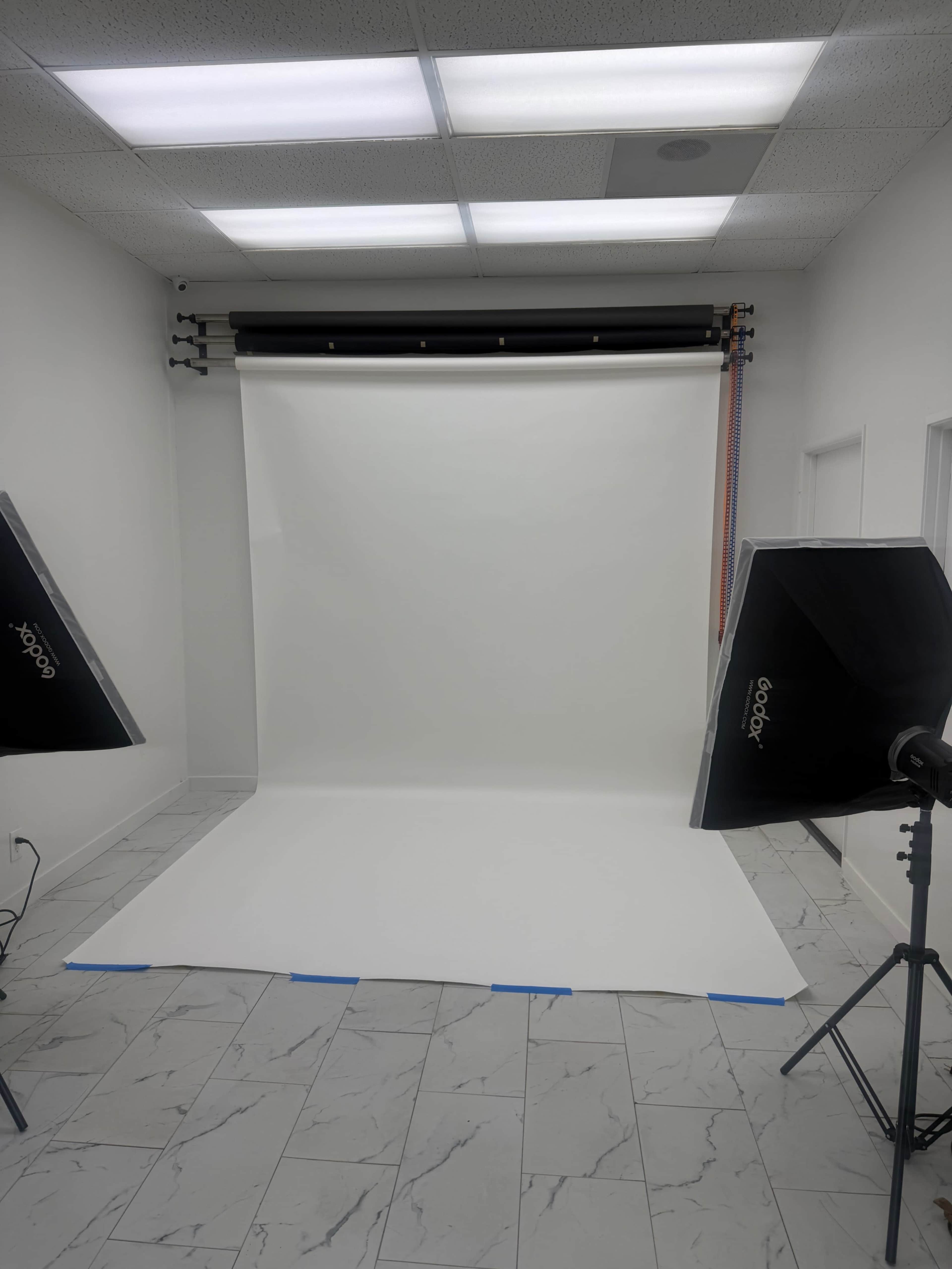 The image shows a well-lit photography studio with a white backdrop and two large softbox lights positioned on either side.