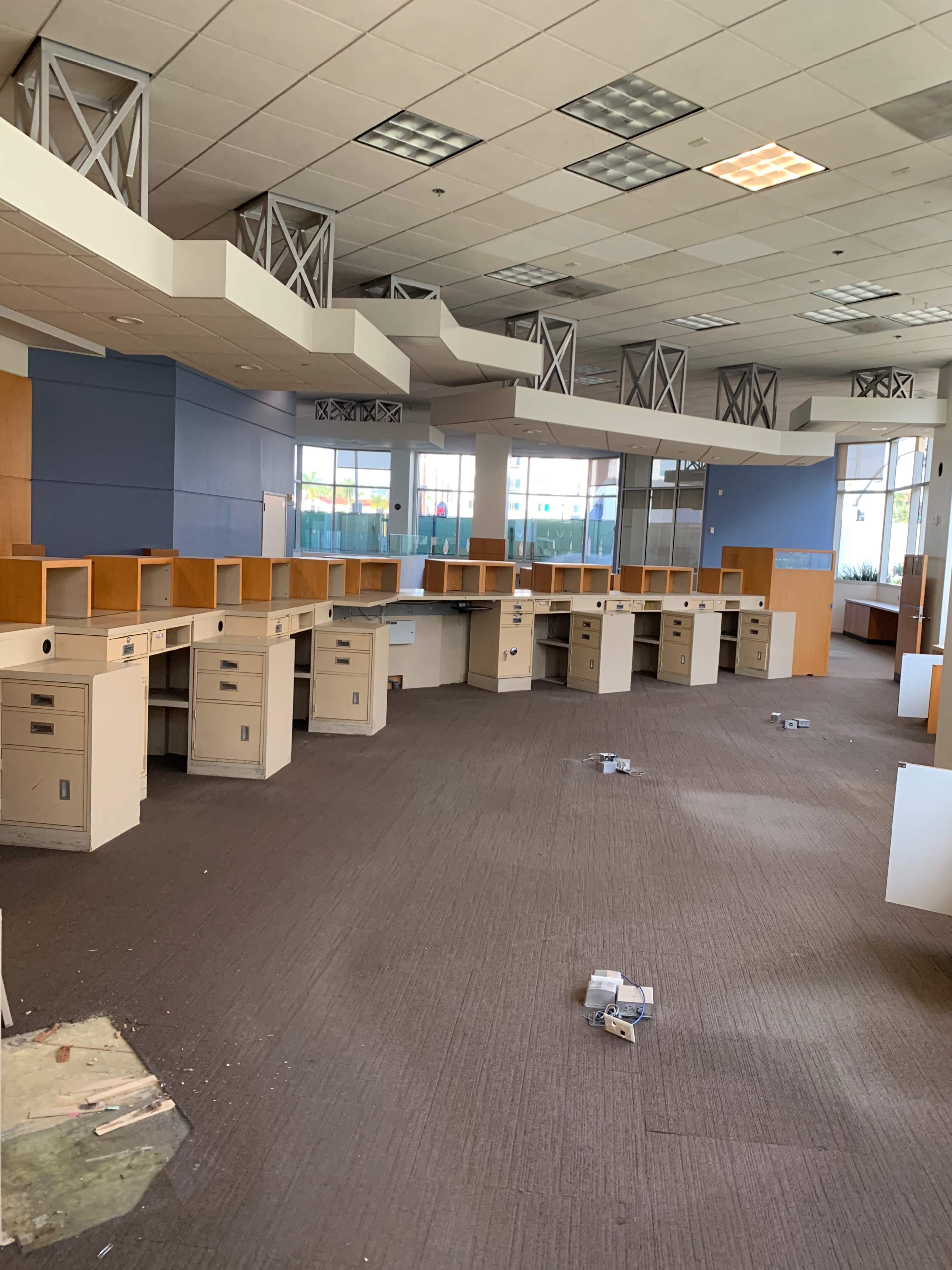The image shows an empty office space with several desks arranged in rows, some of which have papers and debris scattered on the floor.