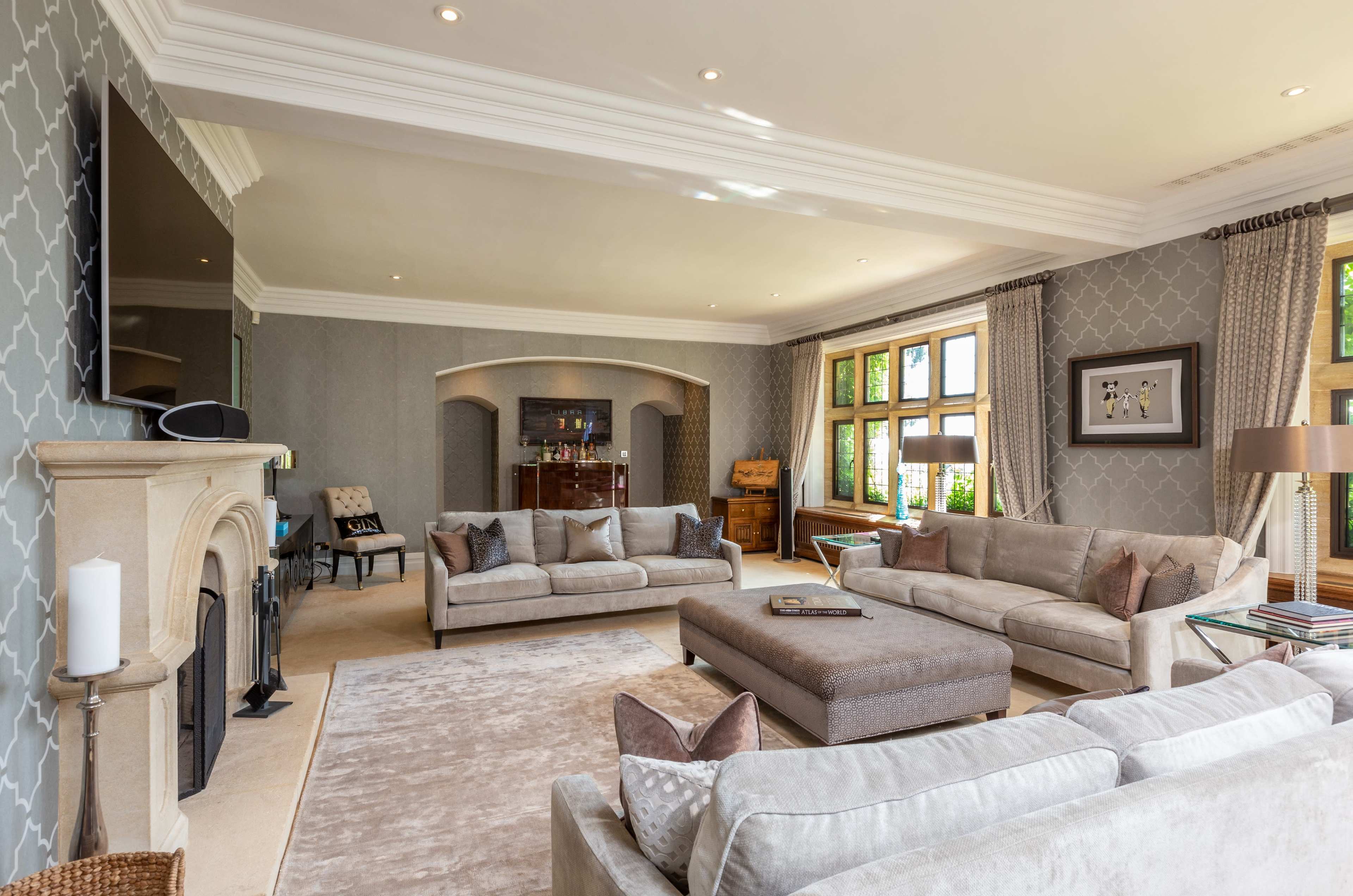 The living room features light-colored sofas arranged around a central coffee table, with large windows allowing natural light to illuminate the space.