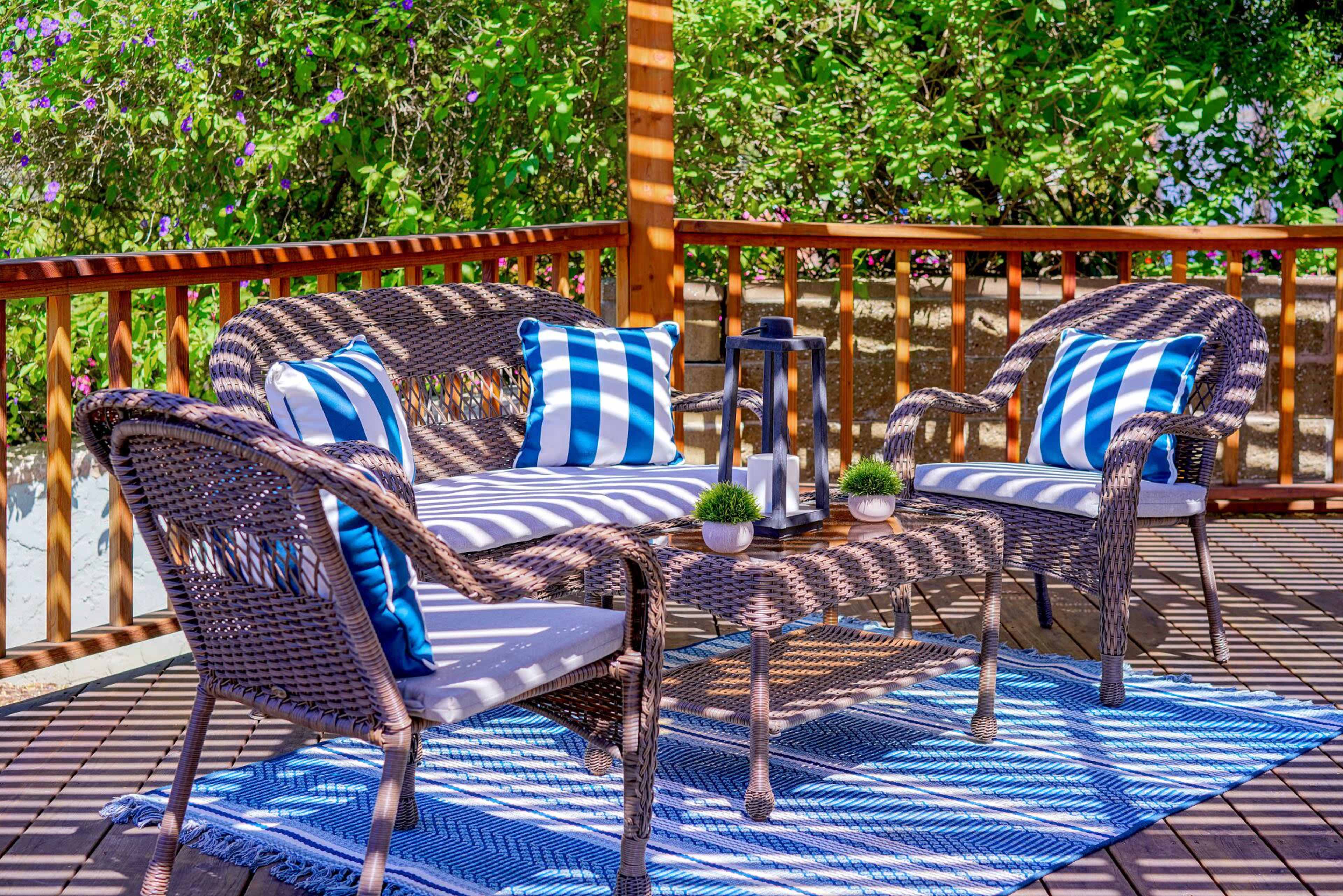 A seating area on a deck features woven furniture with blue and white striped cushions, a coffee table, and small decorative plants.