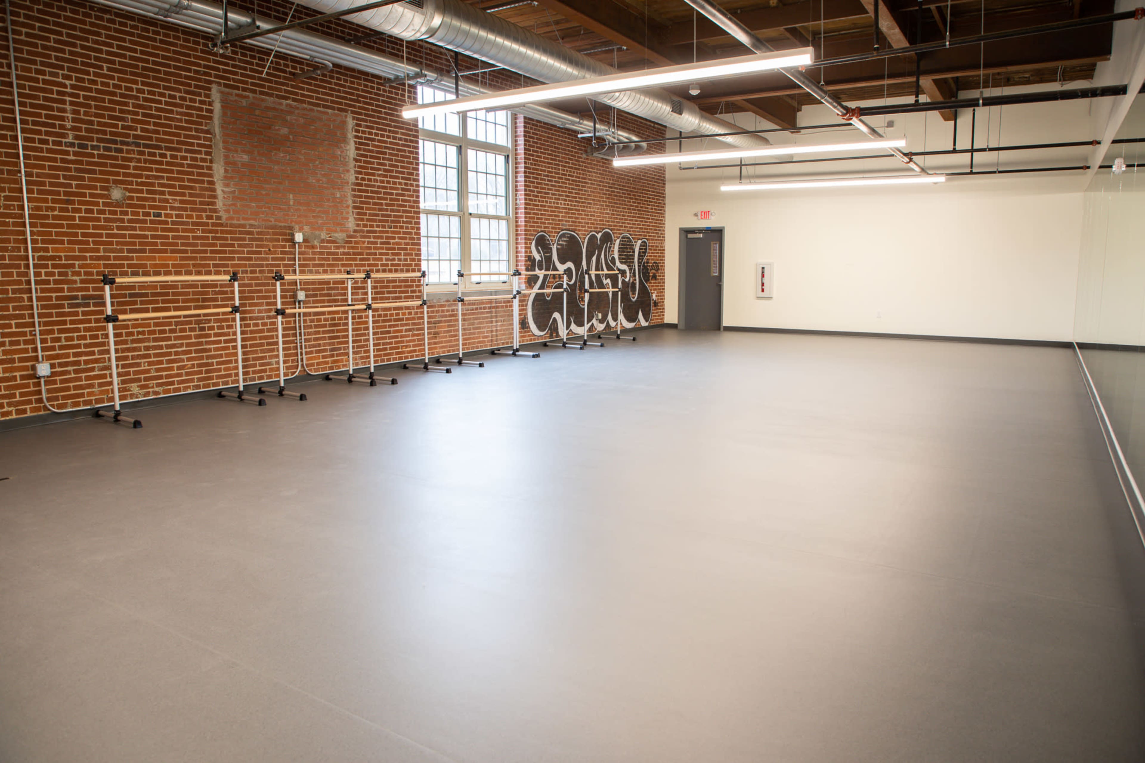 A spacious dance studio with wooden beams, exposed brick walls, and several ballet barres along one side.