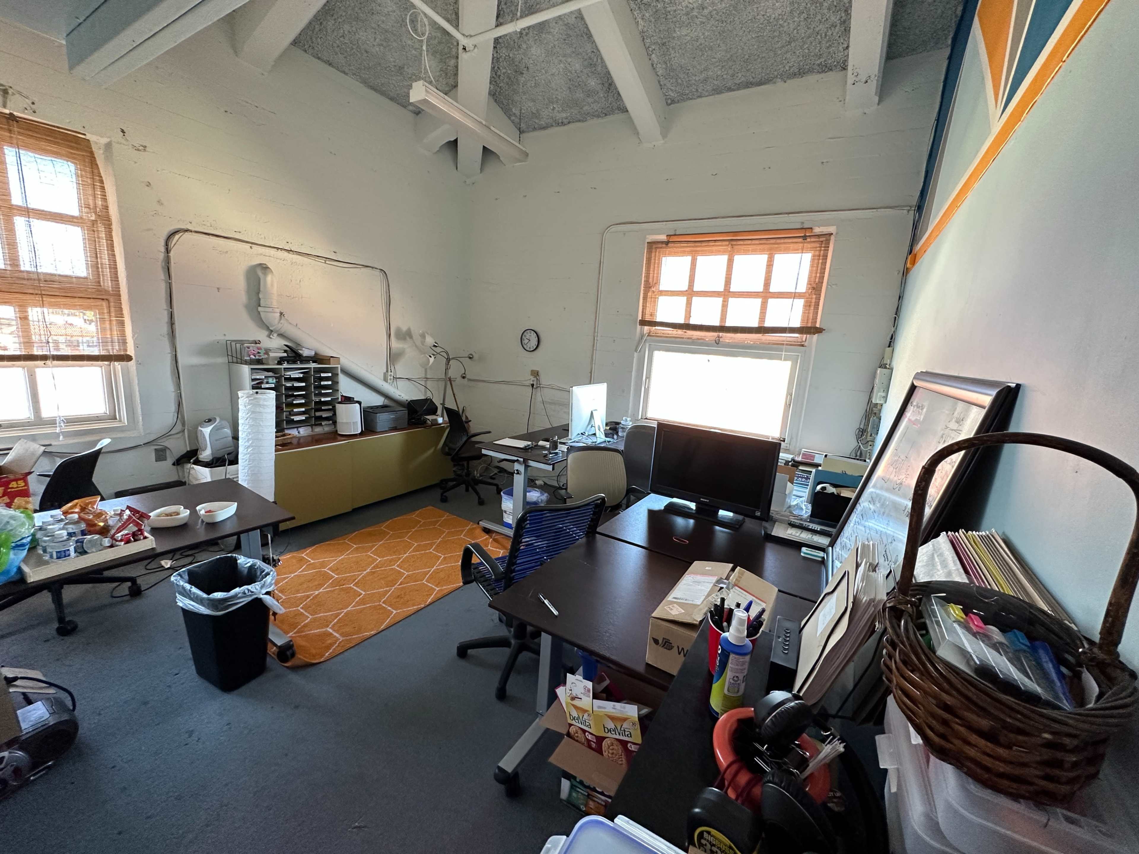 A spacious office with two desks, a filing cabinet, and large windows on opposite walls.