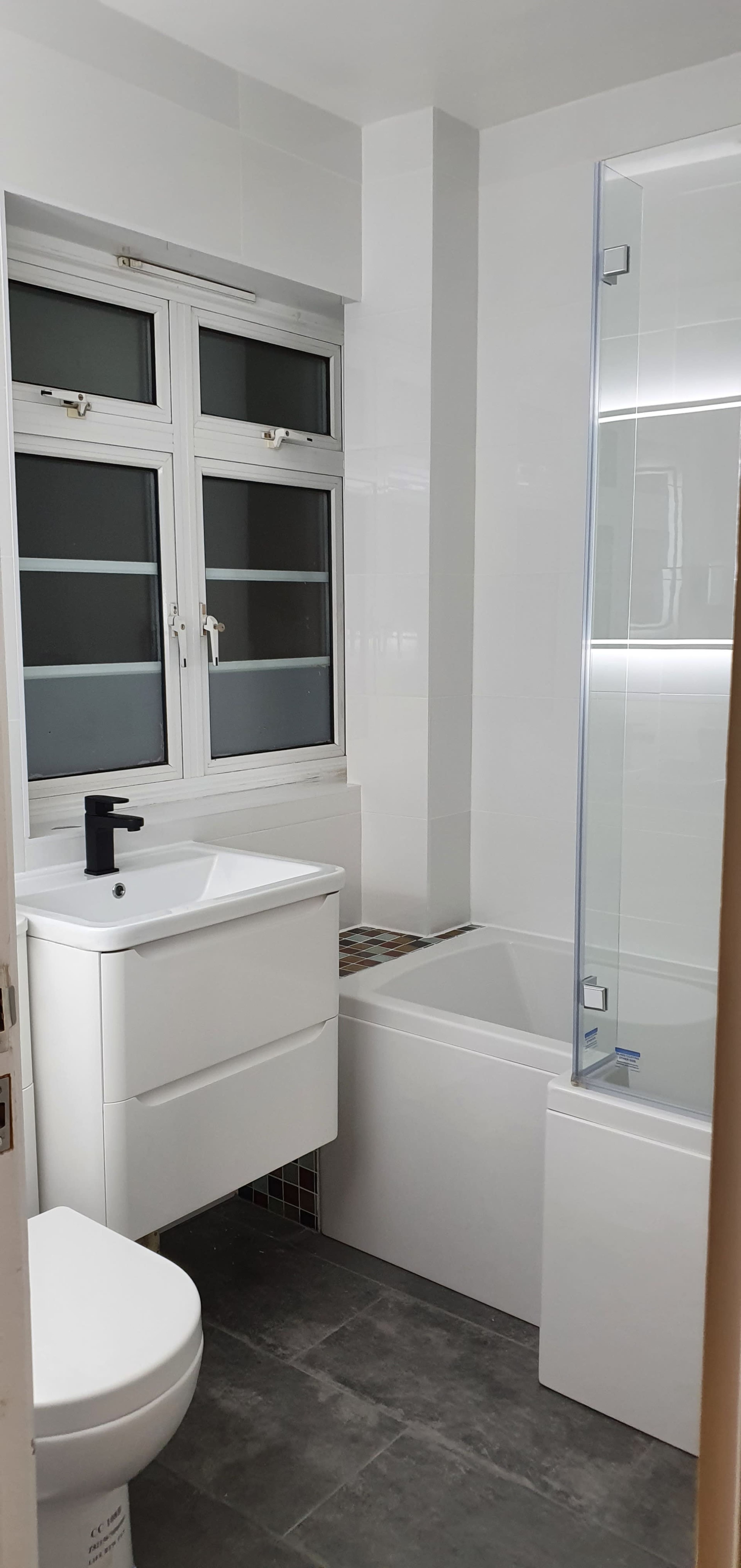 A modern bathroom featuring a bathtub, a sink with a black faucet, and a glass shower enclosure beside a window.