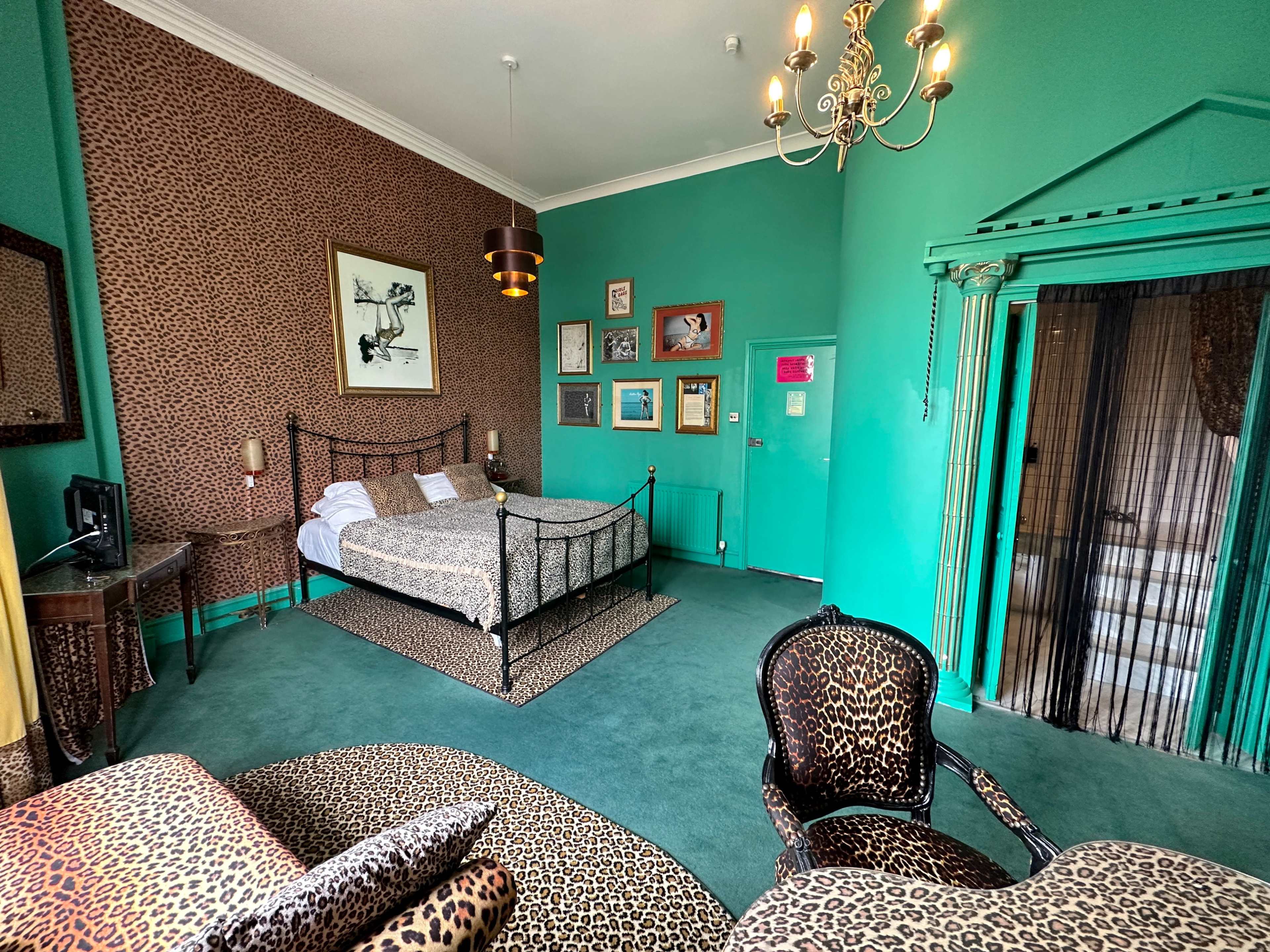 A room decorated with leopard-print furnishings, featuring a bed, a seating area, and vibrant teal walls.