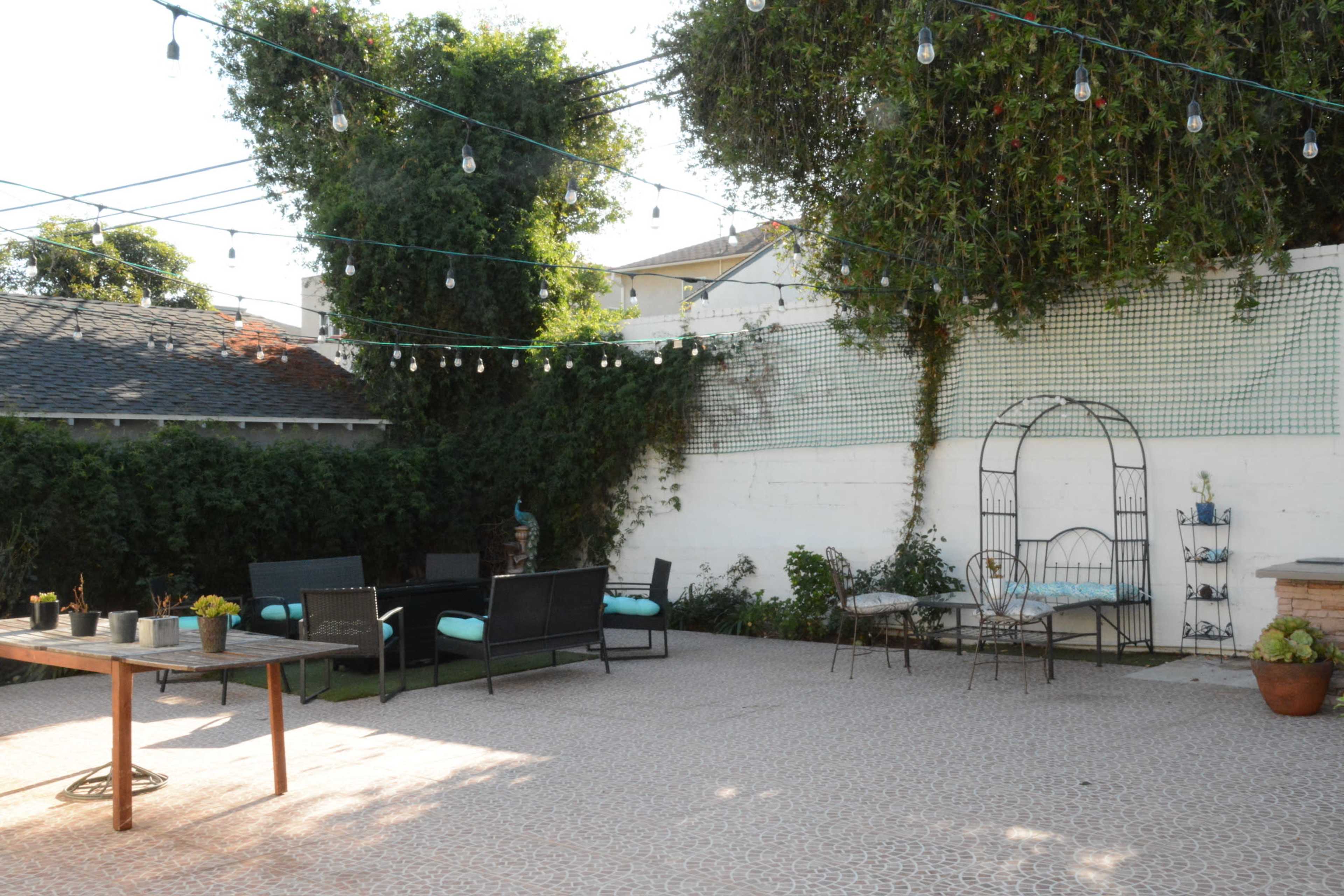 A patio features scattered outdoor furniture, a table with potted plants, and string lights overhead.
