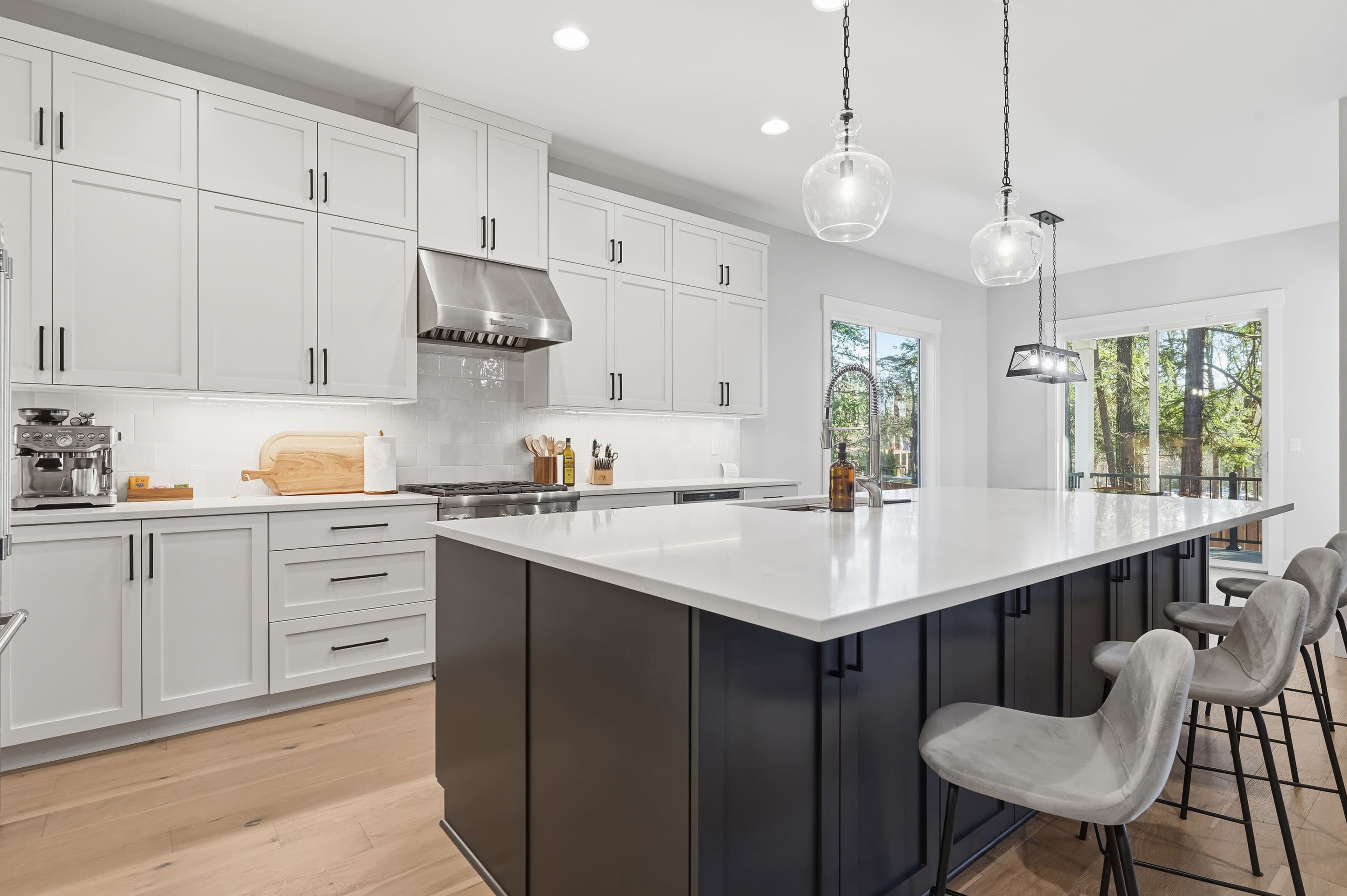 The image shows a modern kitchen featuring white cabinetry, a large island with a dark base, and pendant lighting above.