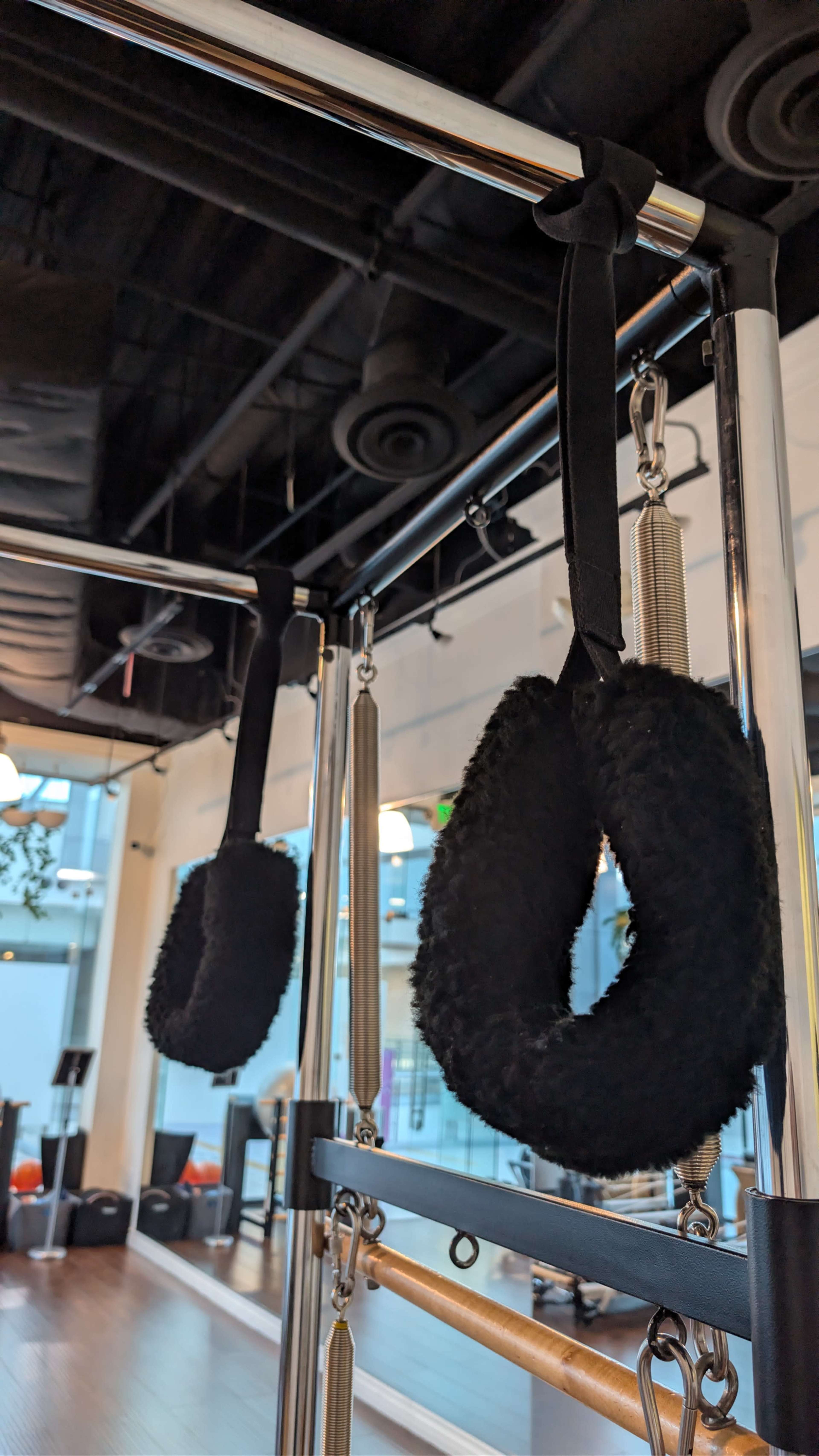 The image features black exercise rings suspended on a metal structure in a fitness studio.