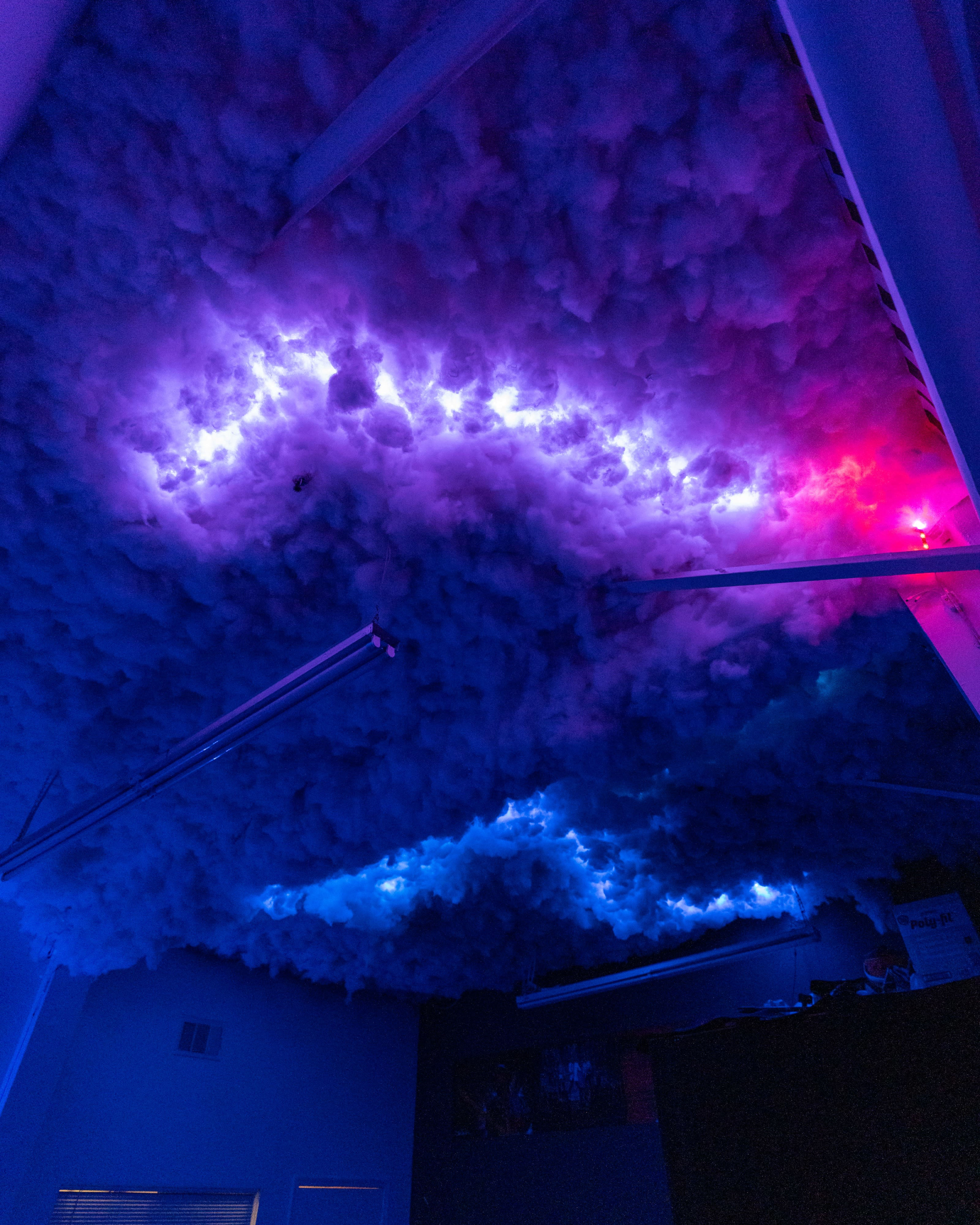 The ceiling features a textured installation of fluffy, cloud-like material illuminated by blue and pink lights.