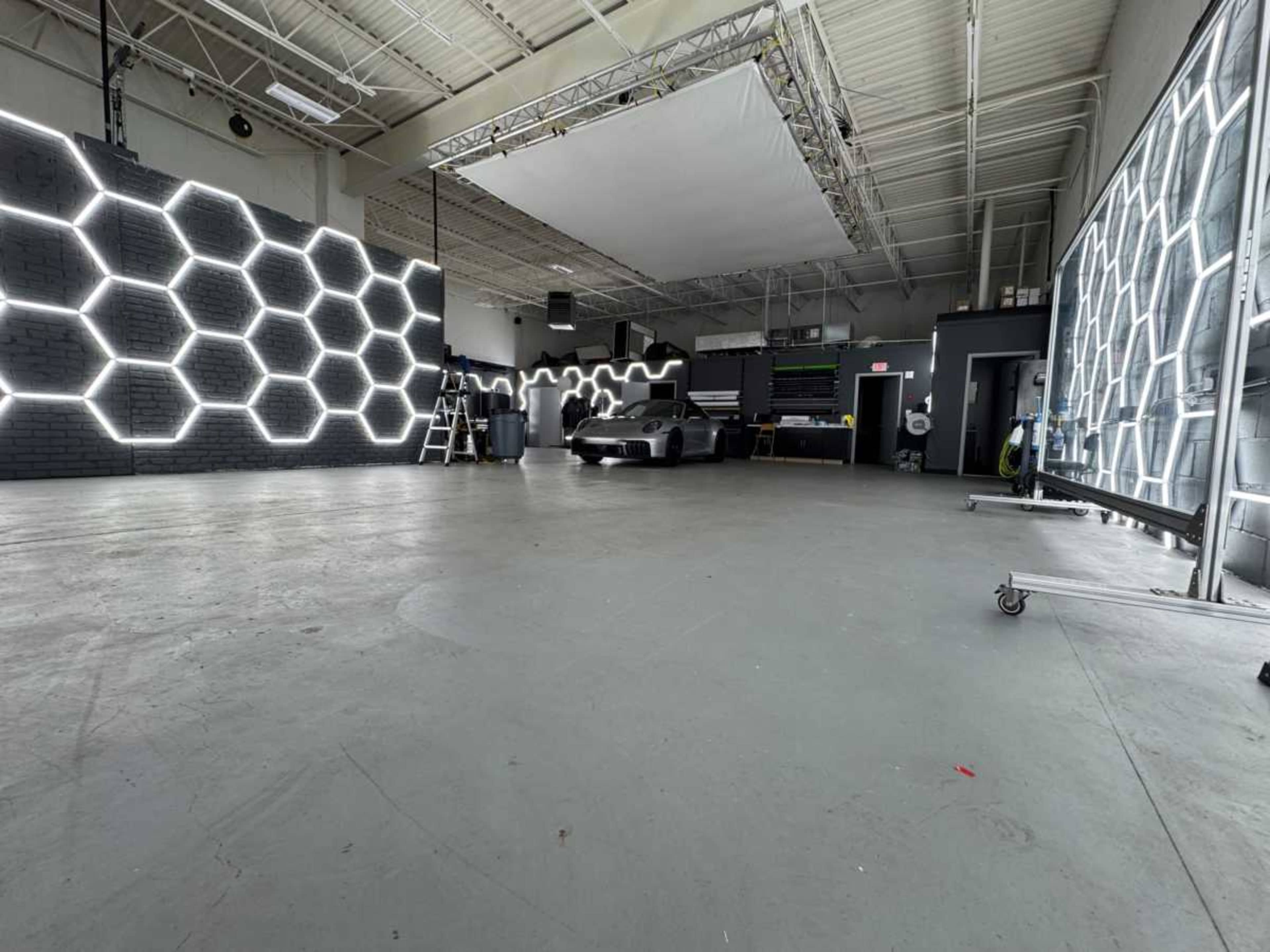 The image shows an empty studio space featuring hexagonal light designs on one wall and a sleek car parked in the center.