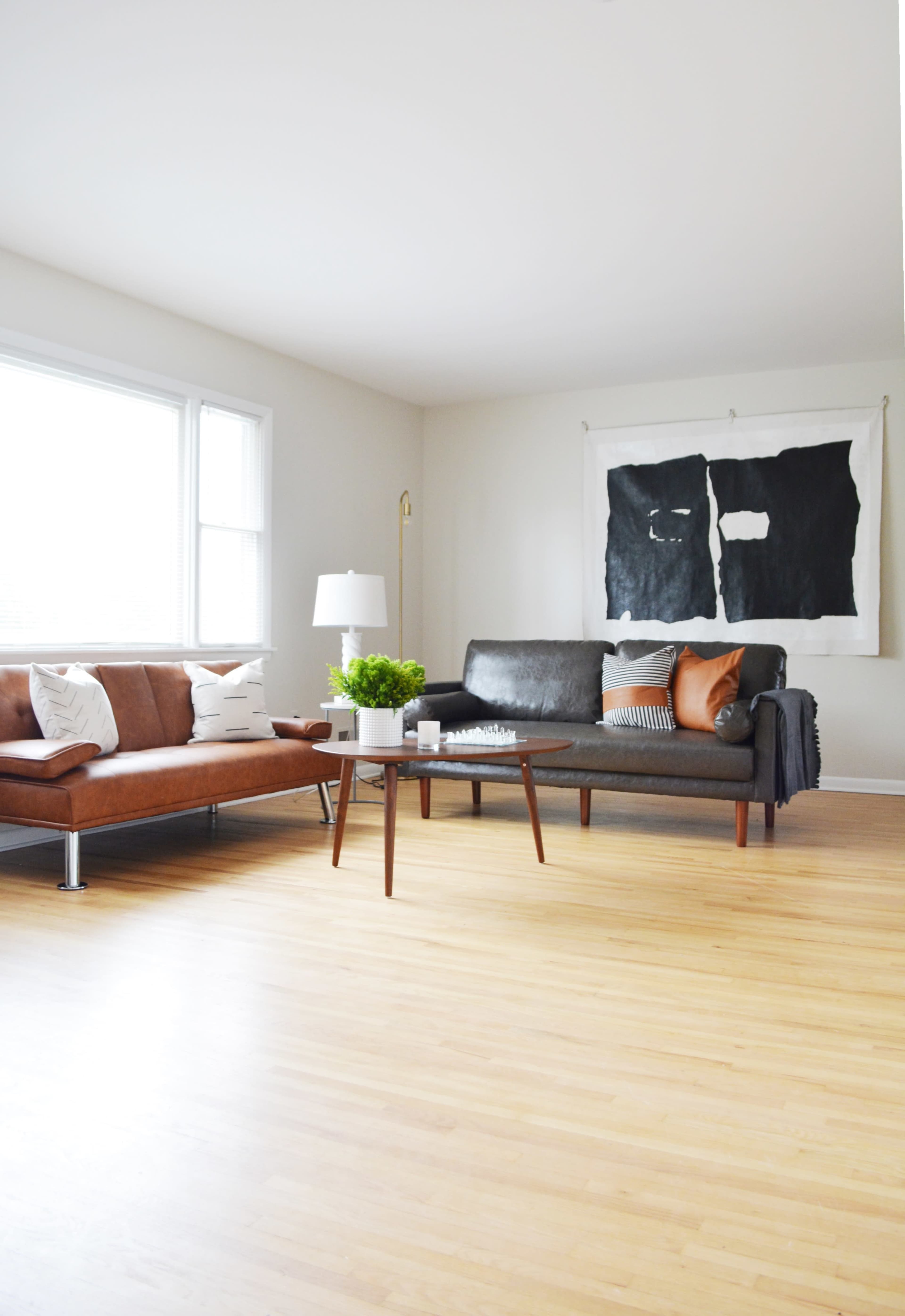 A living room features a brown leather sofa and a black leather couch, accompanied by a coffee table and a large wall art piece.