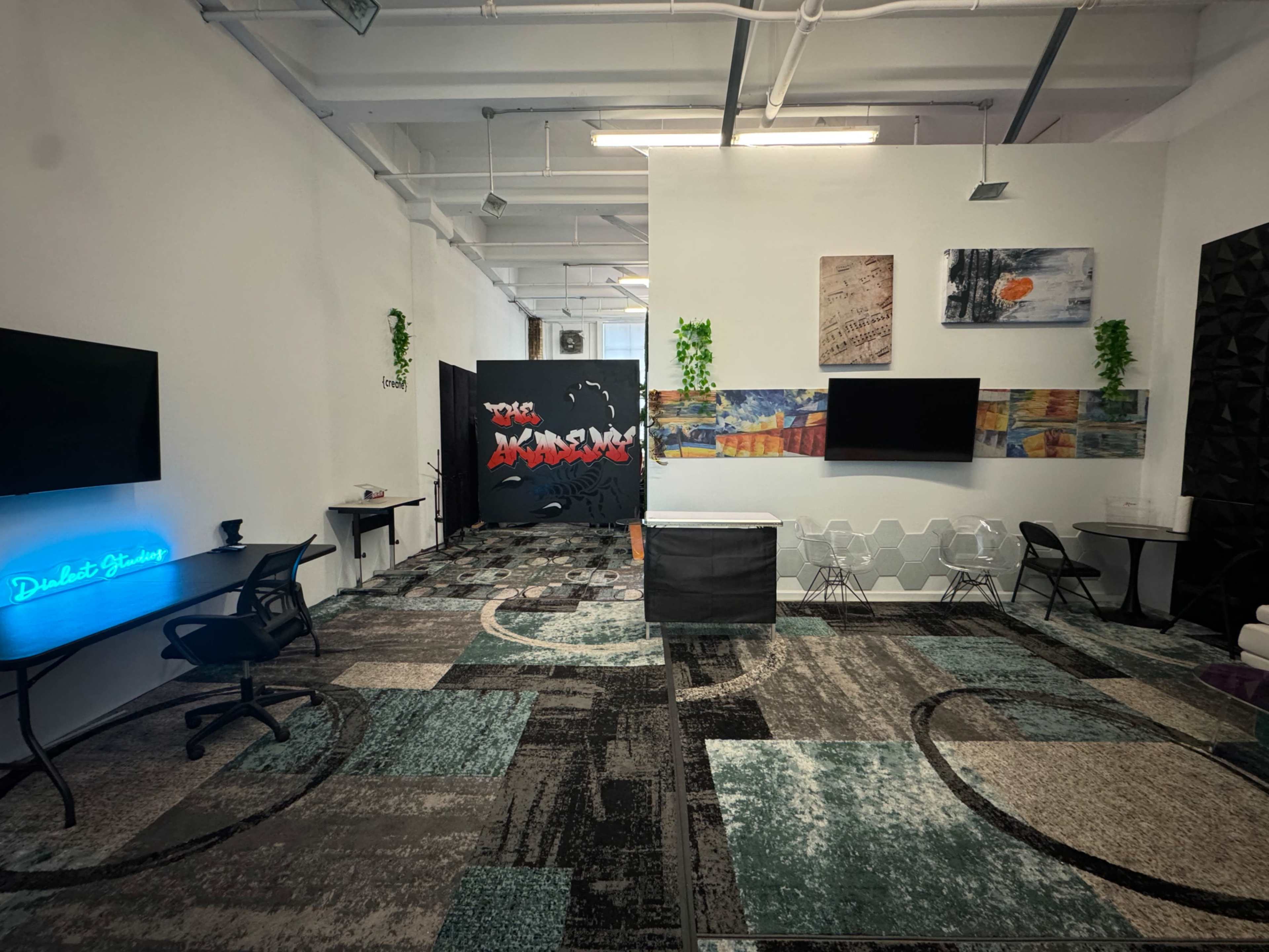 The image shows a modern office space featuring a combination of seating areas, decorative wall panels, and two large screen displays.