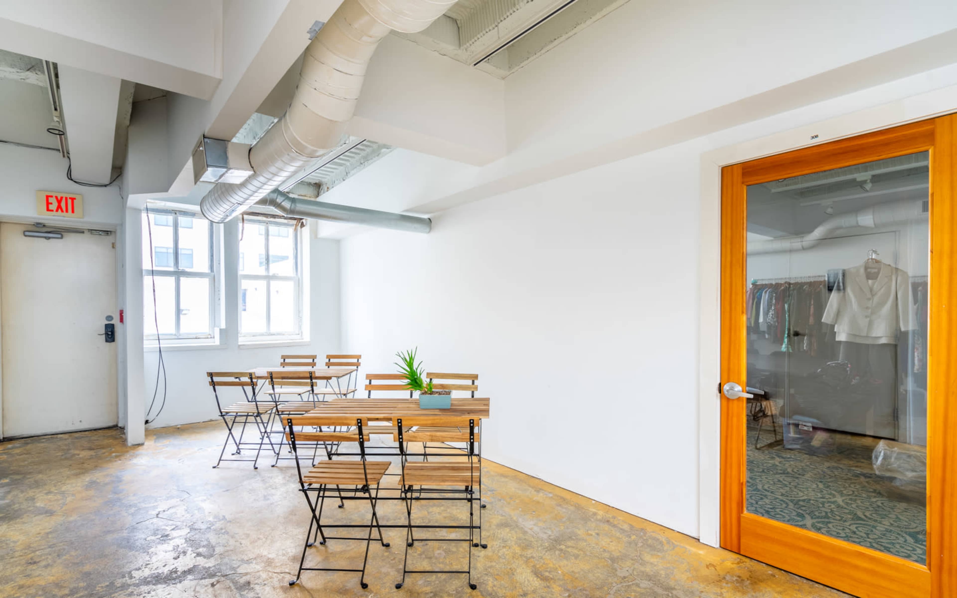 A spacious room features a wooden table with folding chairs, a large glass door, and exposed pipes on the ceiling.