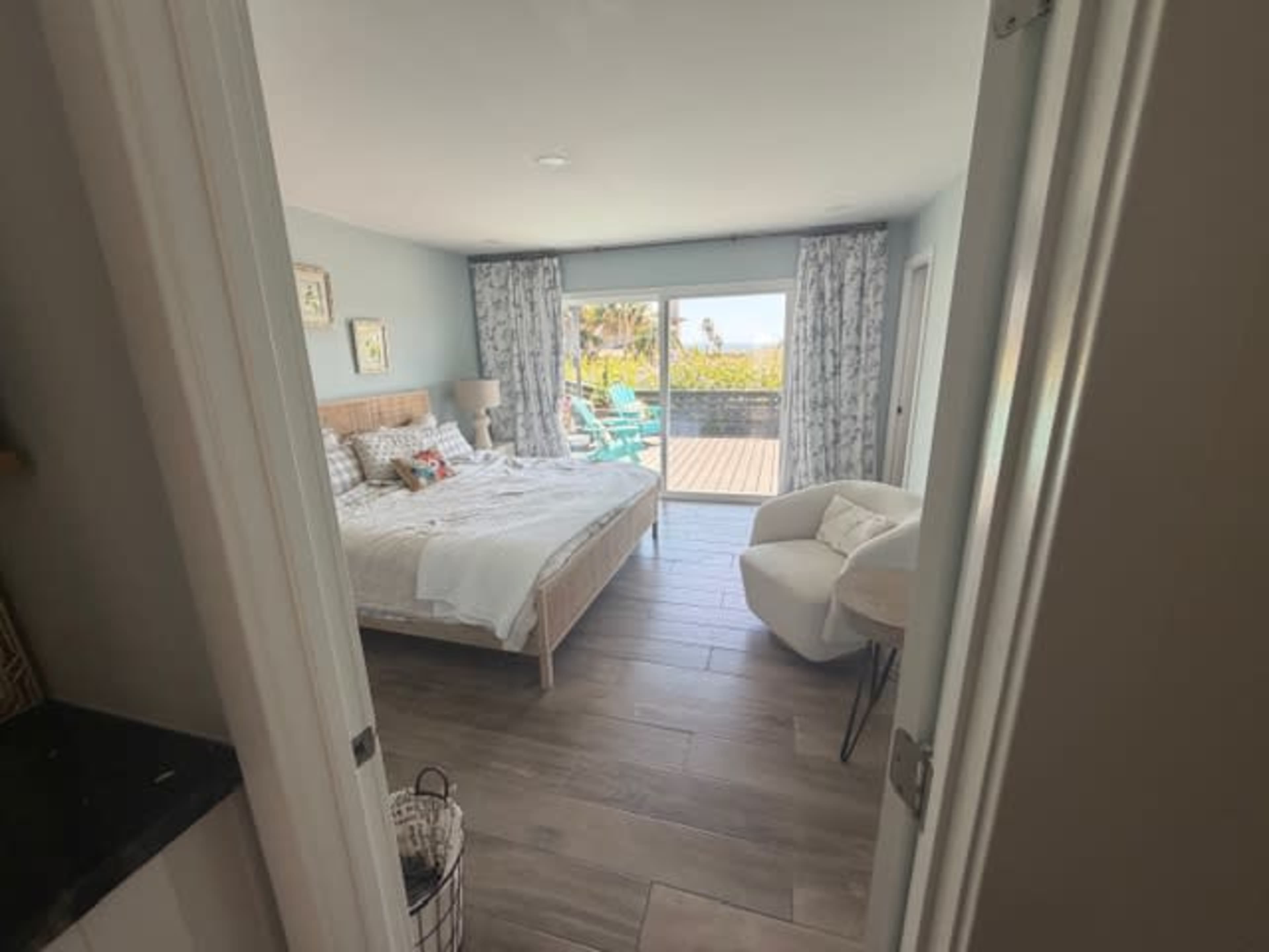 The image shows a bedroom with a bed and chairs, overlooking a patio through sliding glass doors.